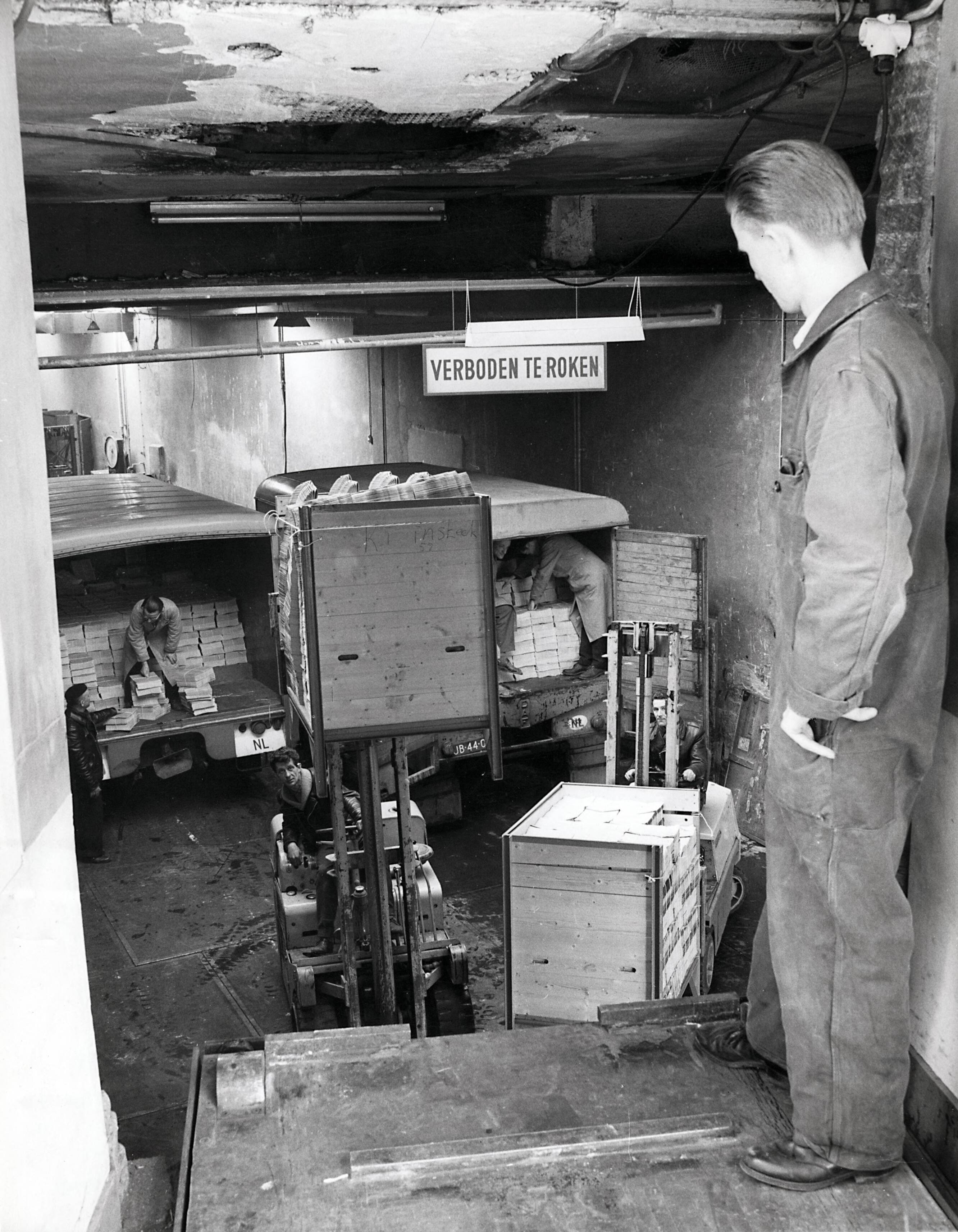 Collectie nader te bepalen — [Serie Bedrijfsvoering Spaarnestad] [expditieruimte, man staat in de uitgifte. Voor hem twee vorkheftruck met kisten met tijdschriften. Achter deze twee vrachtwagens, die worden ingeladen] — Foto: Fotograaf Onbekend / Fotobureau onbekend / Spaarnestad Photo (05887). Licentie: Set B: Rechtenvrij / Publiek Domein. Bron: Nationaal Archief. http://hdl.handle.net/10648/35429da6-42a3-a382-e063-6df0900a6686