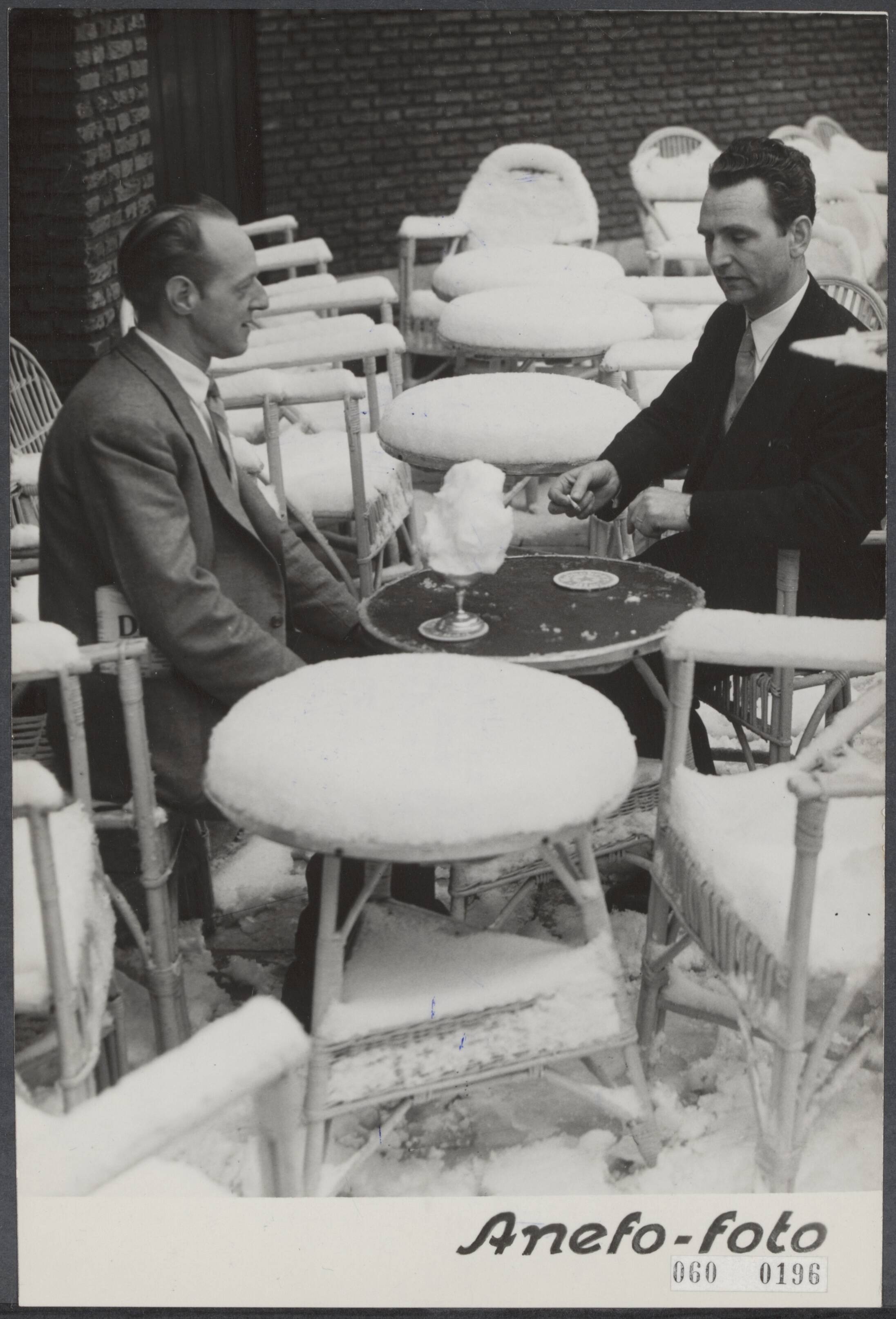 Fotocollectie Elsevier Binnenland — Sneeuw in de lente. Geensceneerde foto. Twee heren op een ondergesneeuwd terras nuttigen een diner — Foto: Duinen, H. van / Anefo. Licentie: Set B: Rechtenvrij / Publiek Domein. Bron: Nationaal Archief. http://hdl.handle.net/10648/ae0d5000-d0b4-102d-bcf8-003048976d84