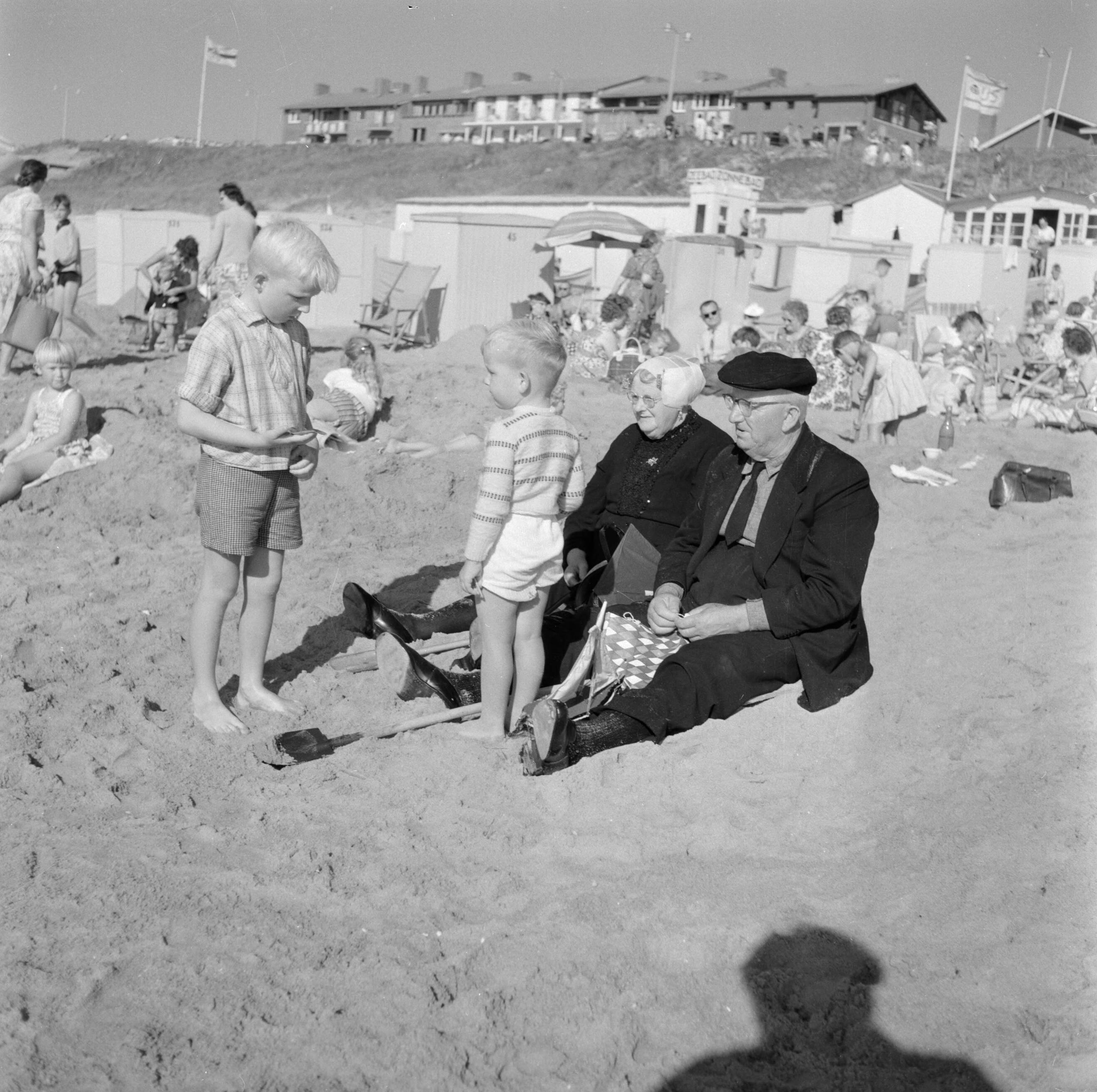 Katwijk — Oud echtpaar in klederdracht met twee jongetjes op het strand — Foto: Poll, Willem van de. Licentie: Set B: Rechtenvrij / Publiek Domein. Bron: Nationaal Archief. http://hdl.handle.net/10648/aed0161c-d0b4-102d-bcf8-003048976d84