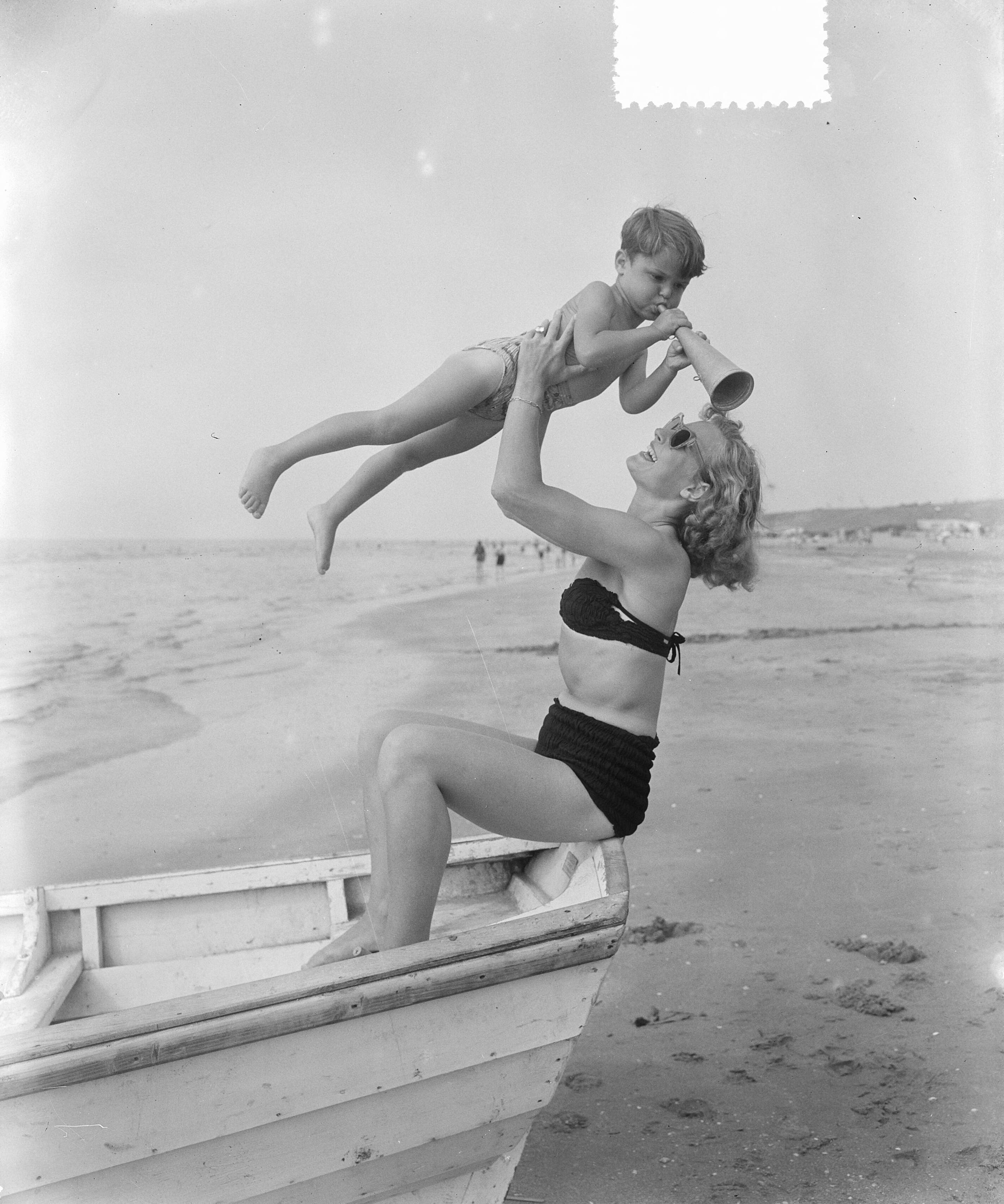 Fotocollectie Anefo — Zomerplaatjes aan strand van Zandvoort. Moeder tilt kind met toeter, zittend in roeiboot — Foto: Pot, Harry / Anefo. Licentie: Set B: Rechtenvrij / Publiek Domein. Bron: Nationaal Archief. http://hdl.handle.net/10648/a90e57de-d0b4-102d-bcf8-003048976d84