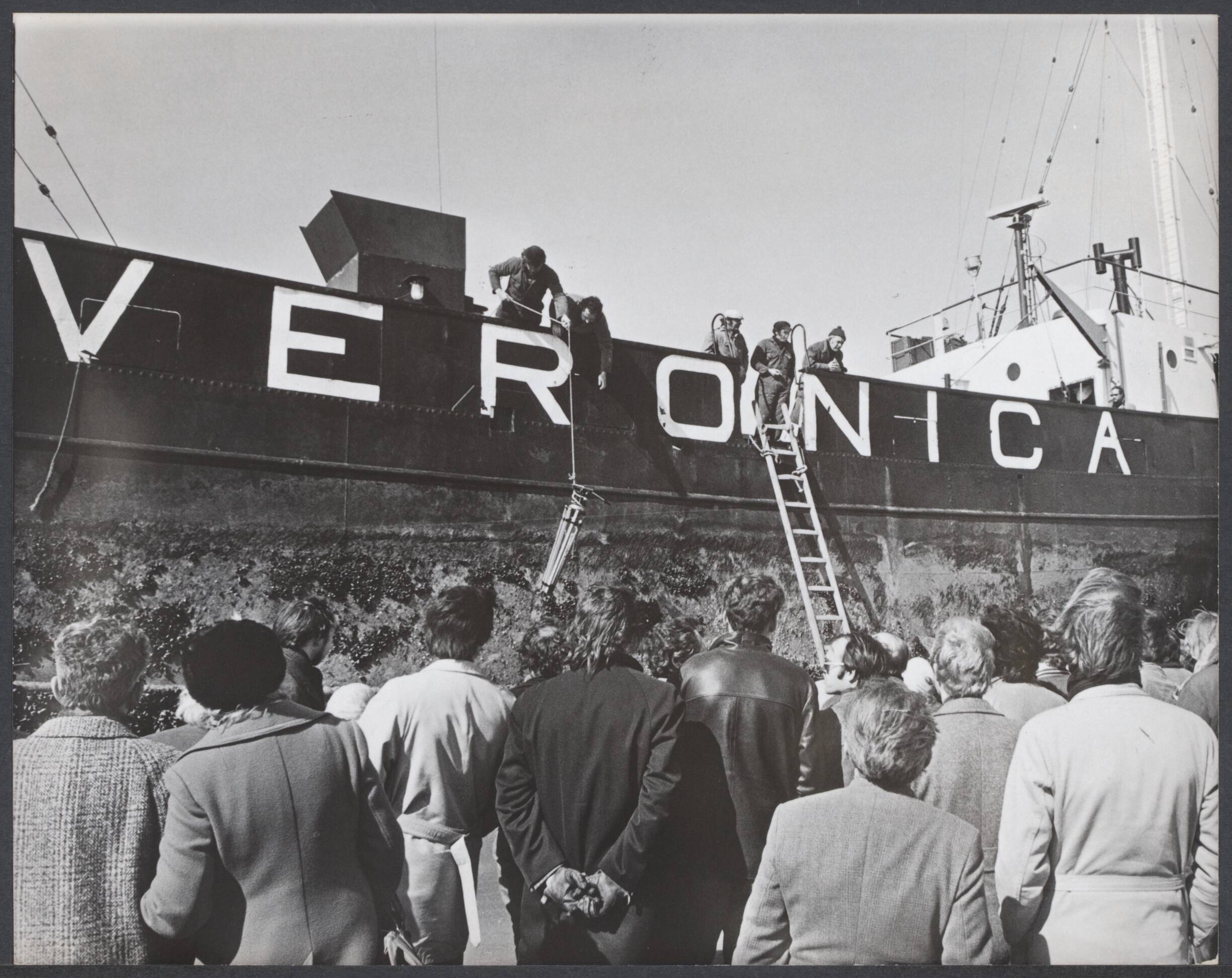Radio Veronica - Nederland — Het schip Veronica gestrand bij Scheveningen na een zware storm op 2 april 1973De weer teruggekeerde bemanning laat bagage op het strand zakken gadegeslagen door honderden nieuwsgierigen — Foto: Verhoeff, Bert / Anefo / ANEFO / NA (04894). Licentie: Set B: Rechtenvrij / Publiek Domein. Bron: Nationaal Archief. http://hdl.handle.net/10648/5900f3c0-7629-45c8-6b69-d25ca72c887e