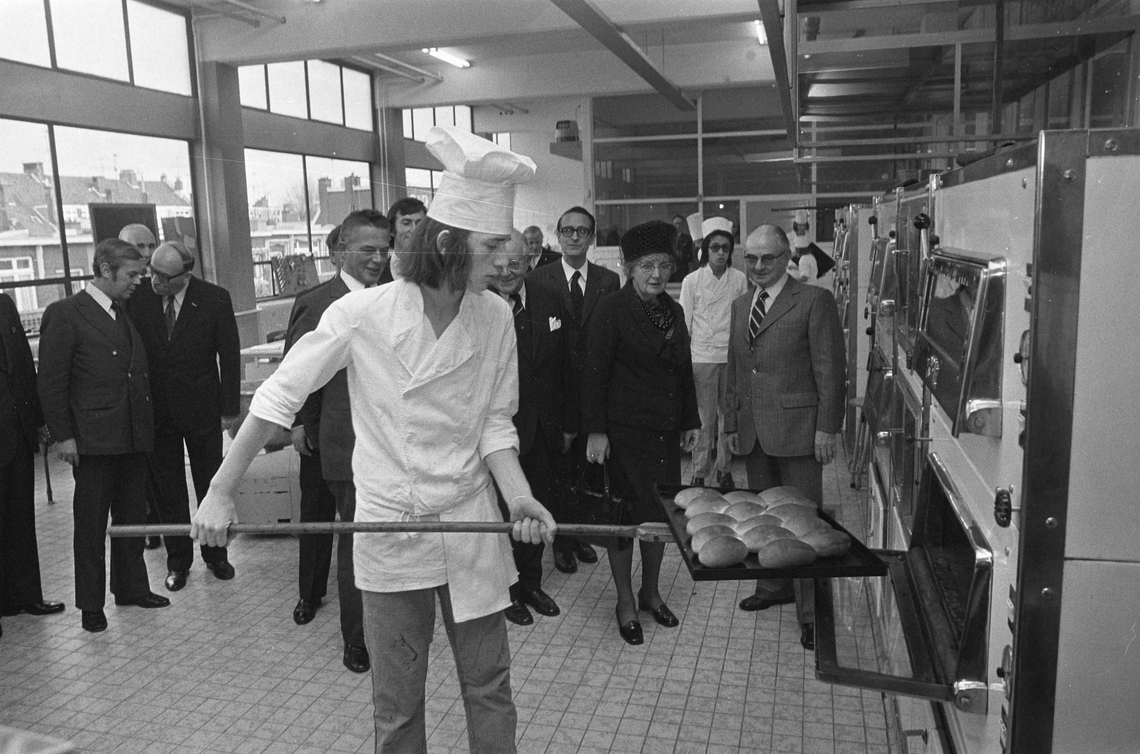 Koningin Juliana bezoekt scholen in Den Haag — De koningin bekijkt een bakker in opleiding in de Vatelschool — Foto: Fotograaf Onbekend / Anefo. Licentie: Set B: Rechtenvrij / Publiek Domein. Bron: Nationaal Archief. http://hdl.handle.net/10648/ac3c3b24-d0b4-102d-bcf8-003048976d84