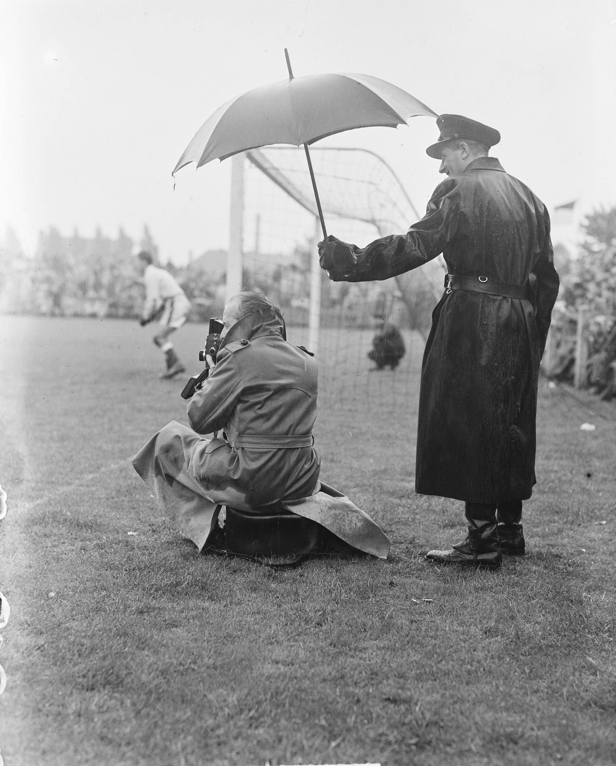 Fotocollectie Anefo — Voetbal. NAC tegen Xerxes 3-2. Fotograaf onder paraplu, vastgehouden door politieagent — Foto: Noske, J.D. / Anefo. Licentie: Set B: Rechtenvrij / Publiek Domein. Bron: Nationaal Archief. http://hdl.handle.net/10648/a8df9dc2-d0b4-102d-bcf8-003048976d84