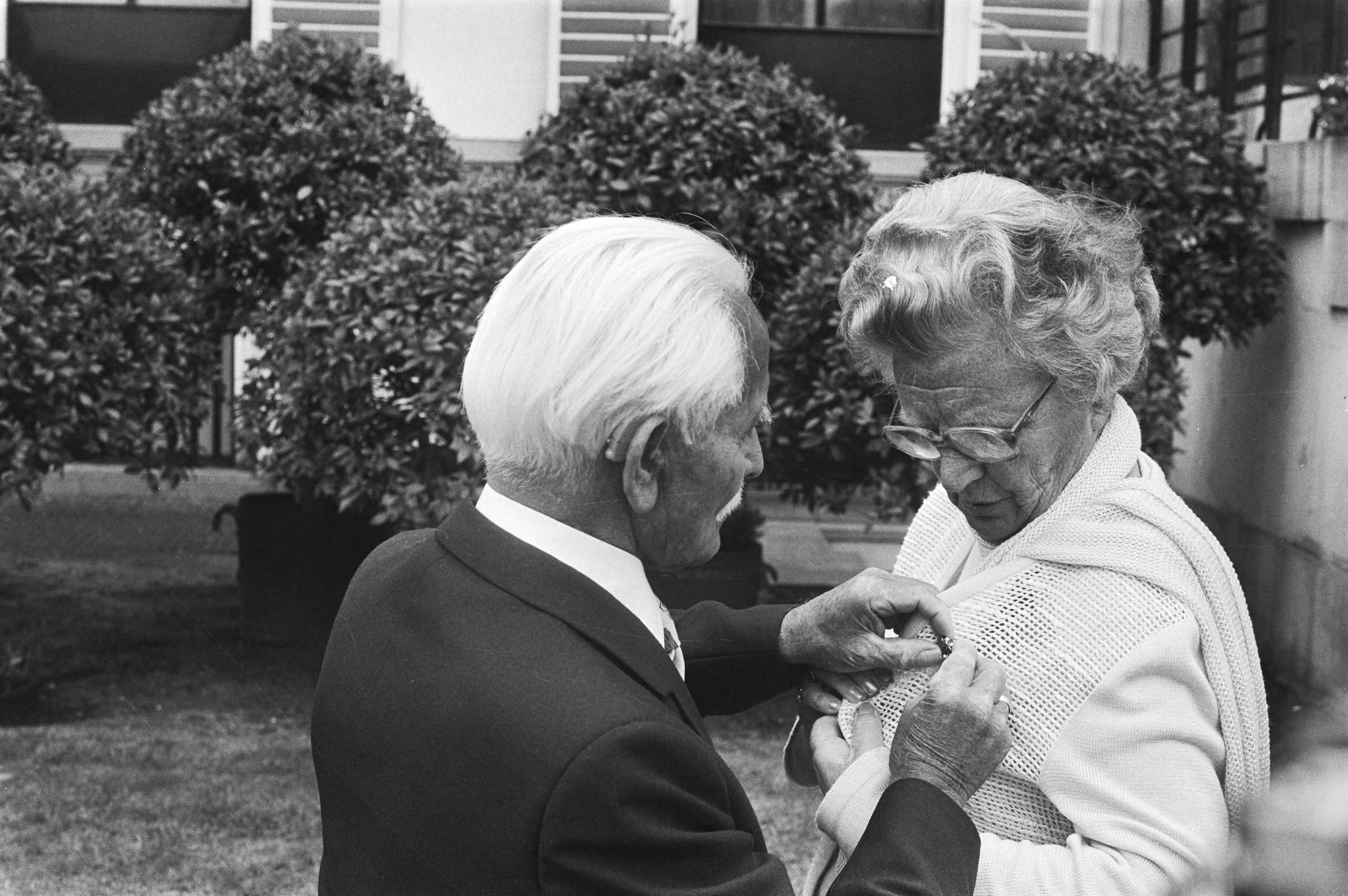 Fotocollectie Anefo — Bejaardendefilé Soestdijk, de 84-jarige heer Wandel speldt koningin Juliana een broche op — Foto: Verhoeff, Bert / Anefo. Licentie: Set B: Rechtenvrij / Publiek Domein. Bron: Nationaal Archief. http://hdl.handle.net/10648/acb624b6-d0b4-102d-bcf8-003048976d84