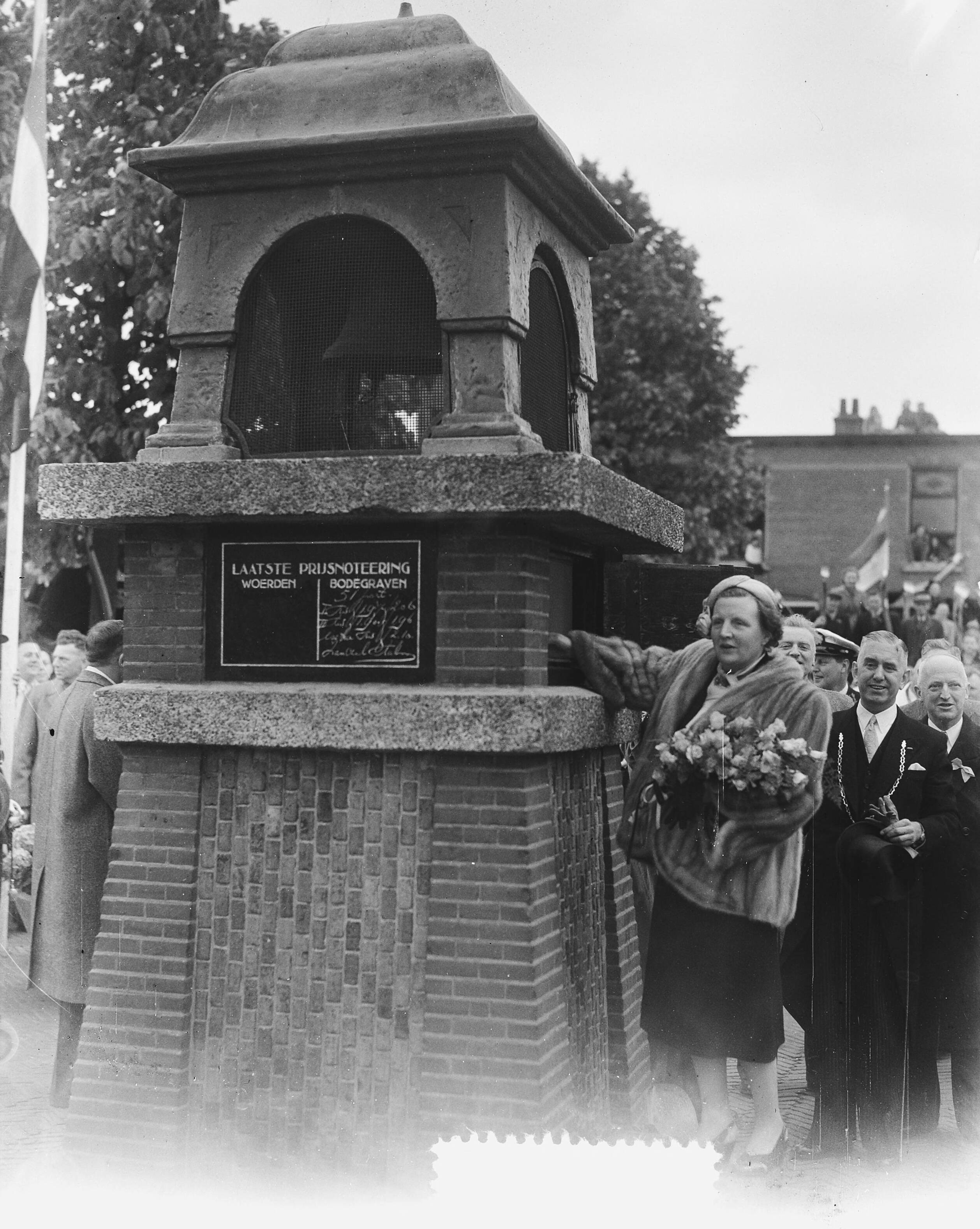 Koninklijk bezoek aan 15 gemeentes in Zuid-Holland (Rijnstreek en Merengebied) — Koningin Juliana en prins Bernhard bezoeken de kaasmarkt in Woerden. Koningin Juliana opent de markt door het negenmaal luiden van een bel — Foto: Noske, J.D. / Anefo. Licentie: Set B: Rechtenvrij / Publiek Domein. Bron: Nationaal Archief. http://hdl.handle.net/10648/a9222958-d0b4-102d-bcf8-003048976d84