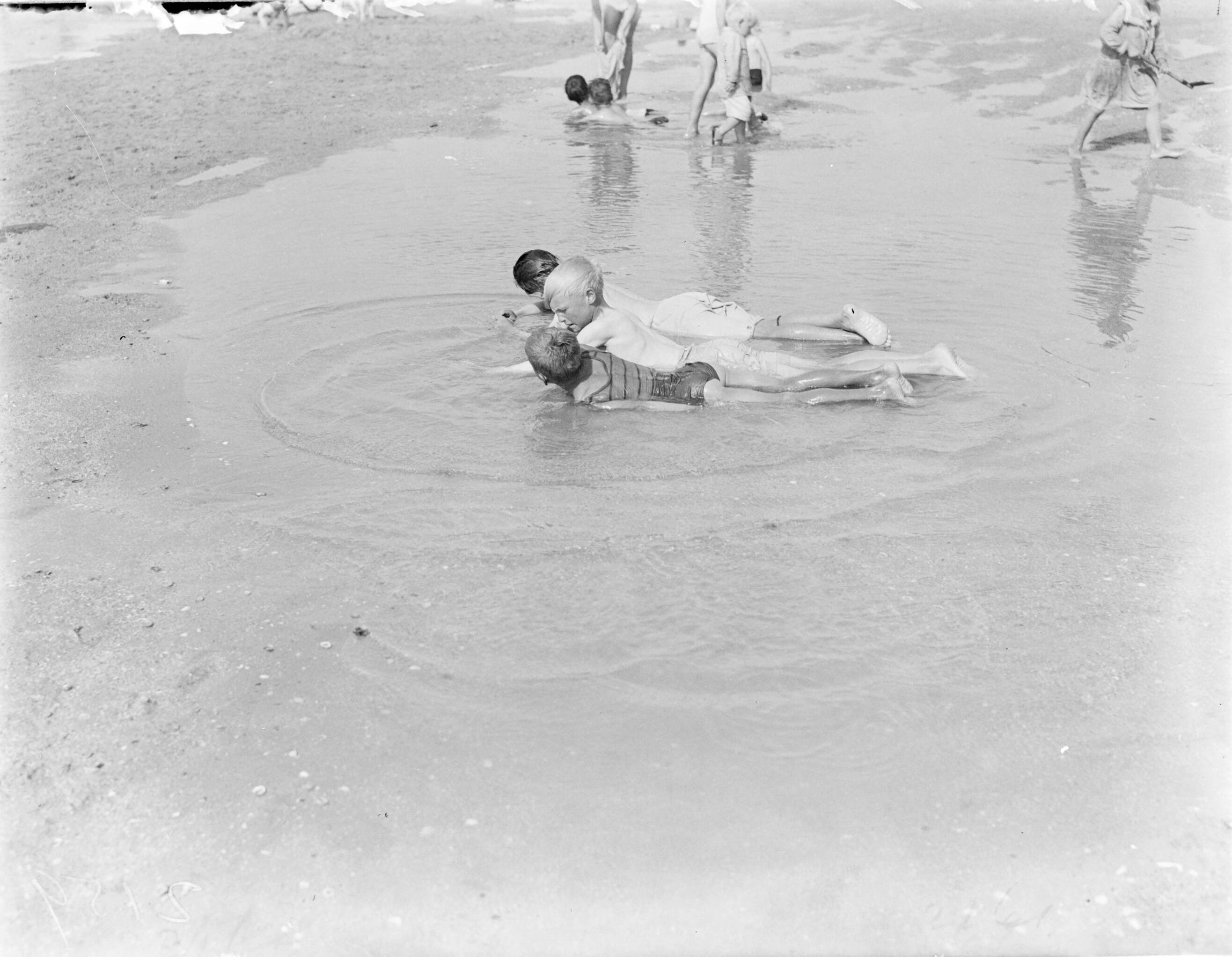 Strandtaferelen Scheveningen — Kinderen liggend in ondiep water — Foto: Poll, Willem van de. Licentie: Set B: Rechtenvrij / Publiek Domein. Bron: Nationaal Archief. http://hdl.handle.net/10648/aea86536-d0b4-102d-bcf8-003048976d84