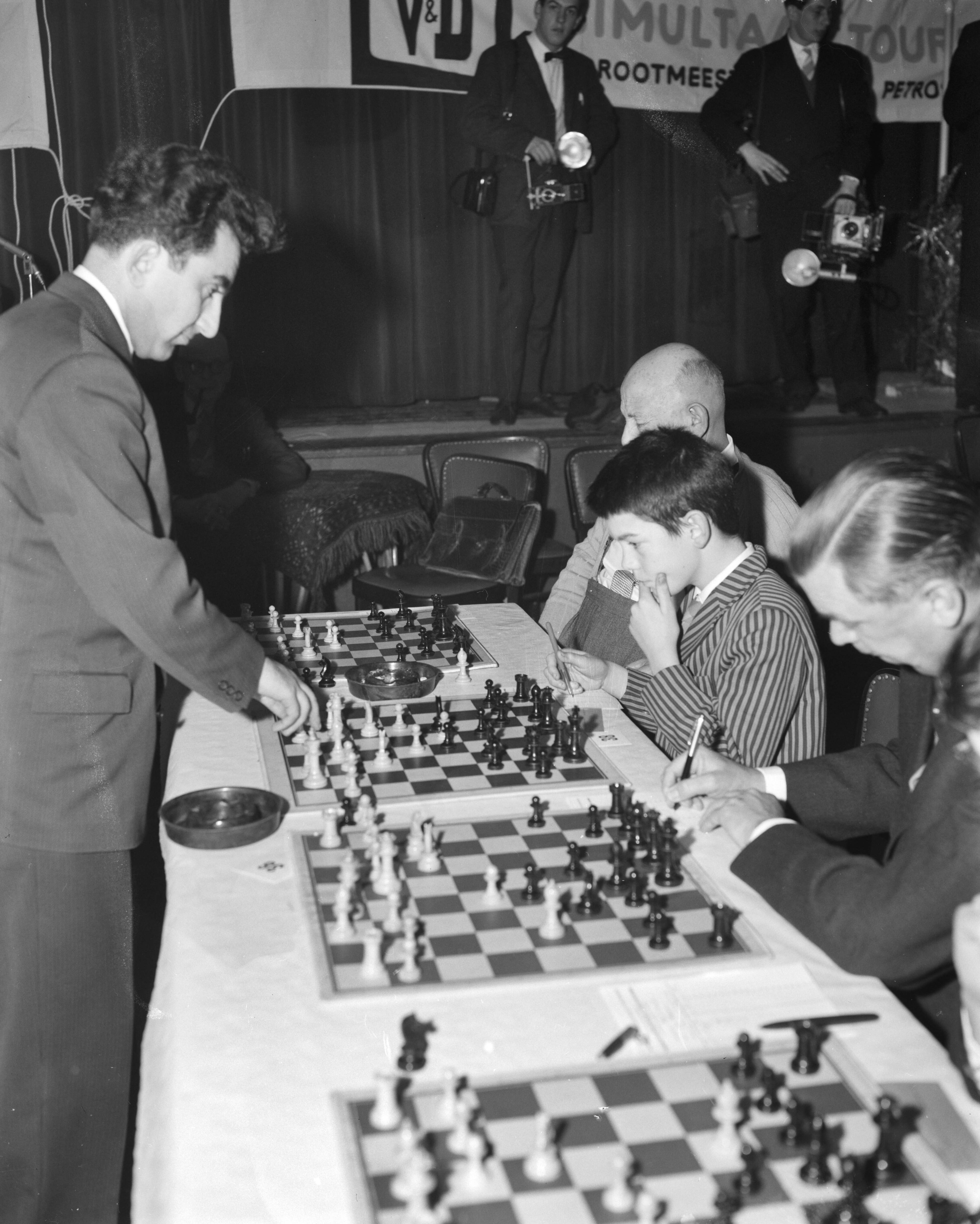 Fotocollectie Anefo — Russische schakers op simultaanschaaktoernooi te Hilversum. Petrosin doet een zet tegen een jonge tegenstander — Foto: Rossem, Wim van / Anefo. Licentie: Set B: Rechtenvrij / Publiek Domein. Bron: Nationaal Archief. http://hdl.handle.net/10648/a9a45d4c-d0b4-102d-bcf8-003048976d84