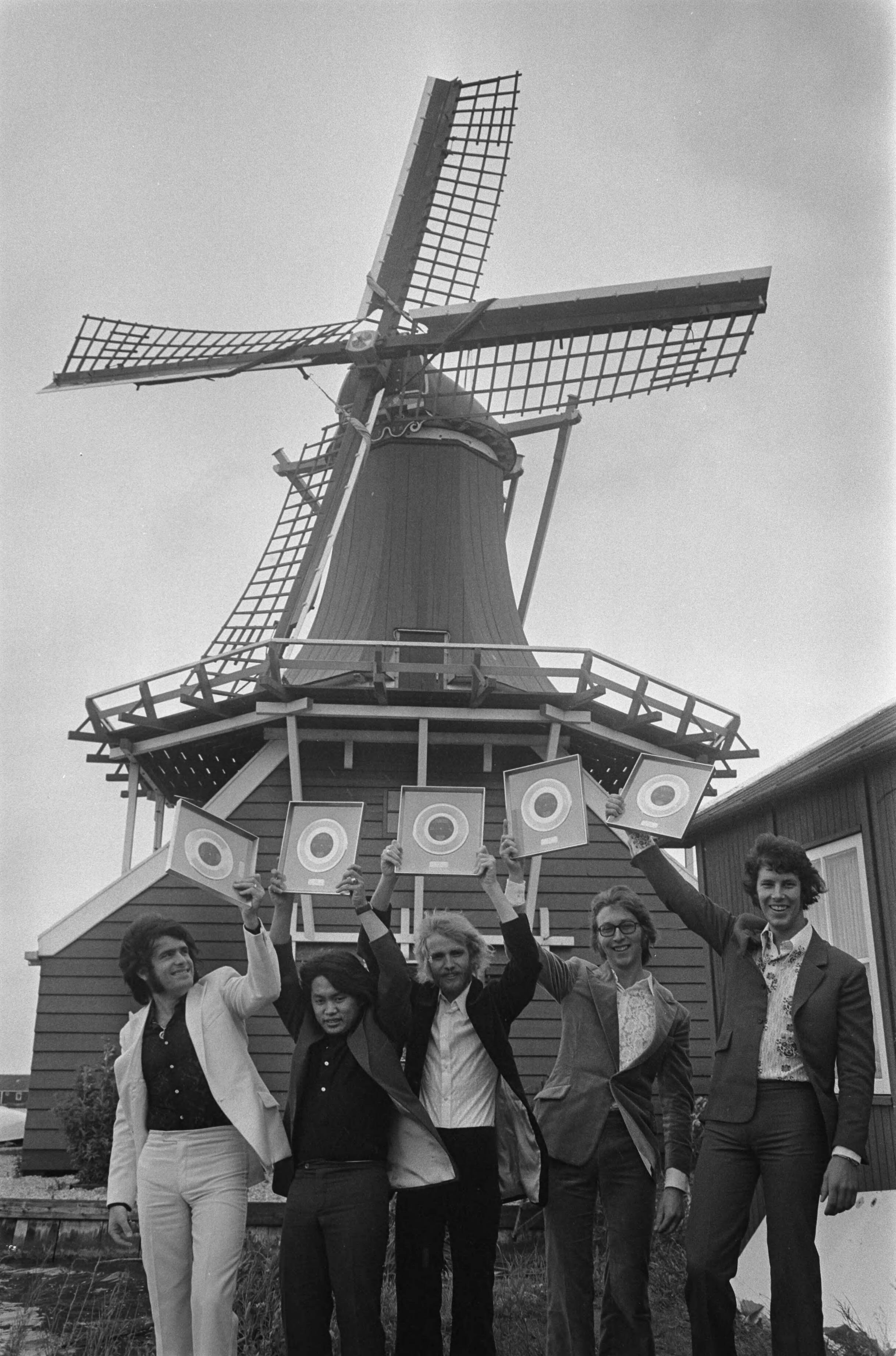 De Zaanse popgroep The George Baker Selection krijgt gouden plaat uitgereikt op de Zaanse Schans — Tegen het decor van de mosterdmolen De Huisman toont de groep zijn net verworven trofee — Foto: Fotograaf Onbekend / Anefo. Licentie: Set B: Rechtenvrij / Publiek Domein. Bron: Nationaal Archief. http://hdl.handle.net/10648/ab9b3fe4-d0b4-102d-bcf8-003048976d84