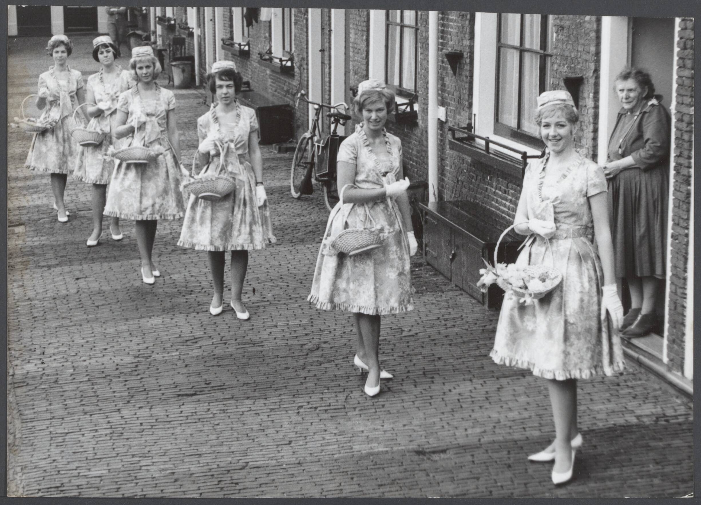 Bloemenmeisjes III — De Haarlemse Bloemenmeisjes werden aan de pers gepresenteerd in hun nieuwe Boussac kantoene jurkjes met groen vilten jassen. Zij zullen, 24 in getal, vanaf 21 maart wanneer de lente begint als gastvrouwen voor Haarlem optreden. Enkele meisjes waaonder Carla, Adri, Inez, Iris en Pien op een der straatjes in het Proveniershofje in Haarlem — Foto: Nijs, Jac. de / Anefo. Licentie: Set B: Rechtenvrij / Publiek Domein. Bron: Nationaal Archief. http://hdl.handle.net/10648/79f8f3e7-6e7d-cd29-c10b-530c41623530