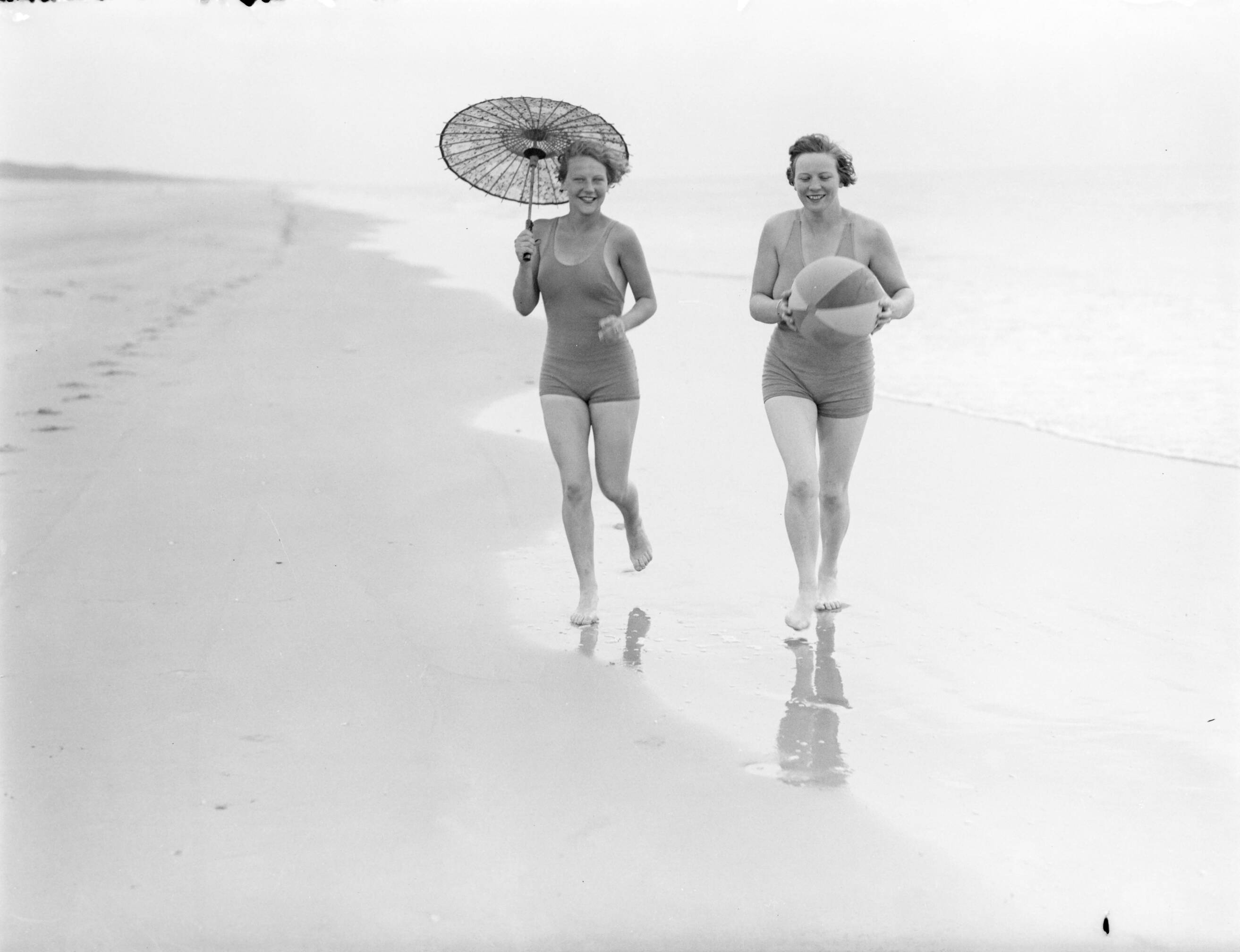 Reportage fotomodel — Model Eva Waldschmidt (met parasol) en Van de Polls vrouw Nell Langlais lopen langs de vloedlijn in Zandvoort — Foto: Poll, Willem van de. Licentie: Set B: Rechtenvrij / Publiek Domein. Bron: Nationaal Archief. http://hdl.handle.net/10648/aea7ff4c-d0b4-102d-bcf8-003048976d84