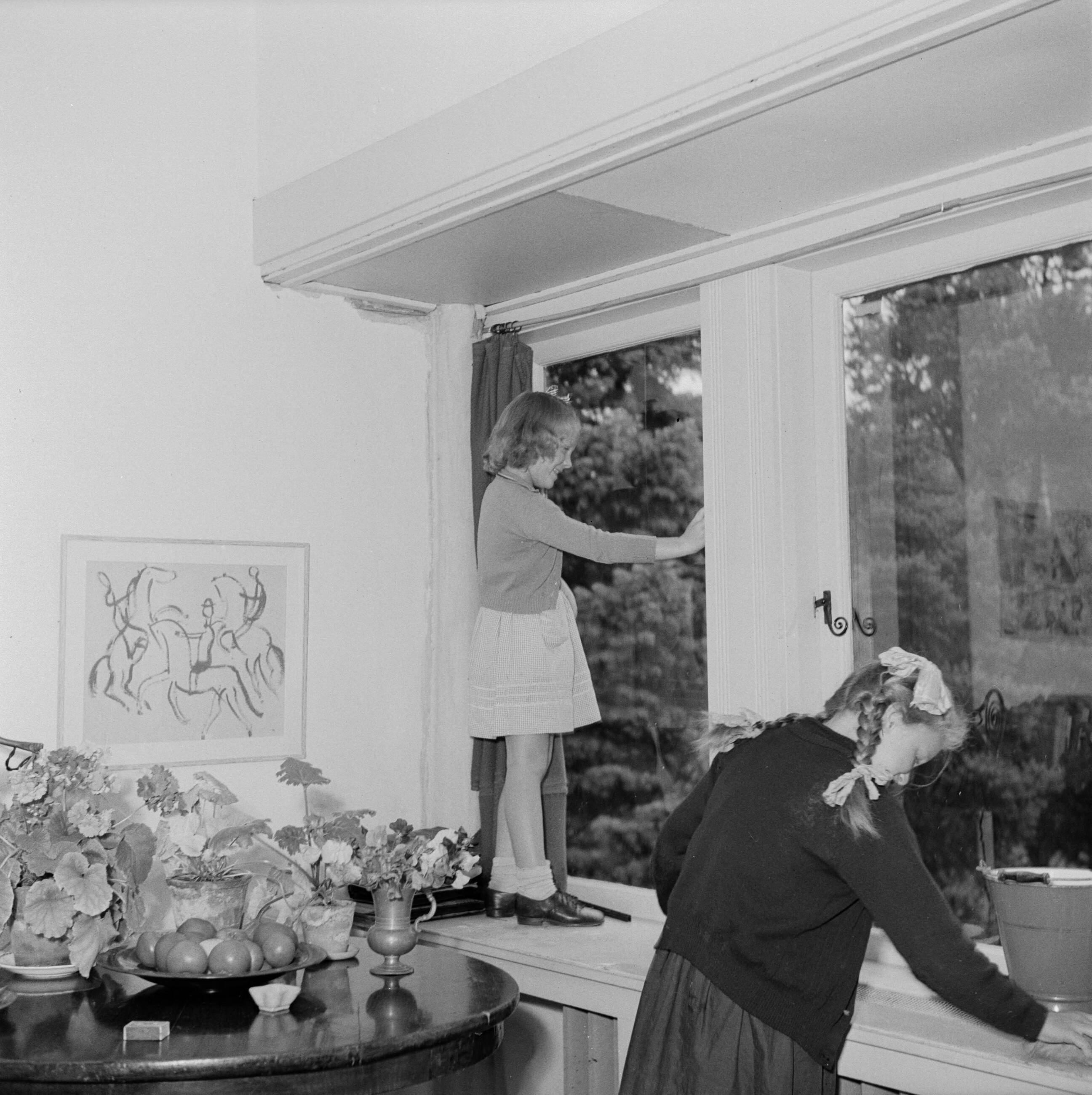 Prinses Beatrix en prinses Irene op de Werkplaats Kindergemeenschap van Kees Boeke te Bilthoven — Prinses Irene poetst, staande op de vensterbank, een raam — Foto: Poll, Willem van de. Licentie: Set B: Rechtenvrij / Publiek Domein. Bron: Nationaal Archief. http://hdl.handle.net/10648/aee81fdc-d0b4-102d-bcf8-003048976d84