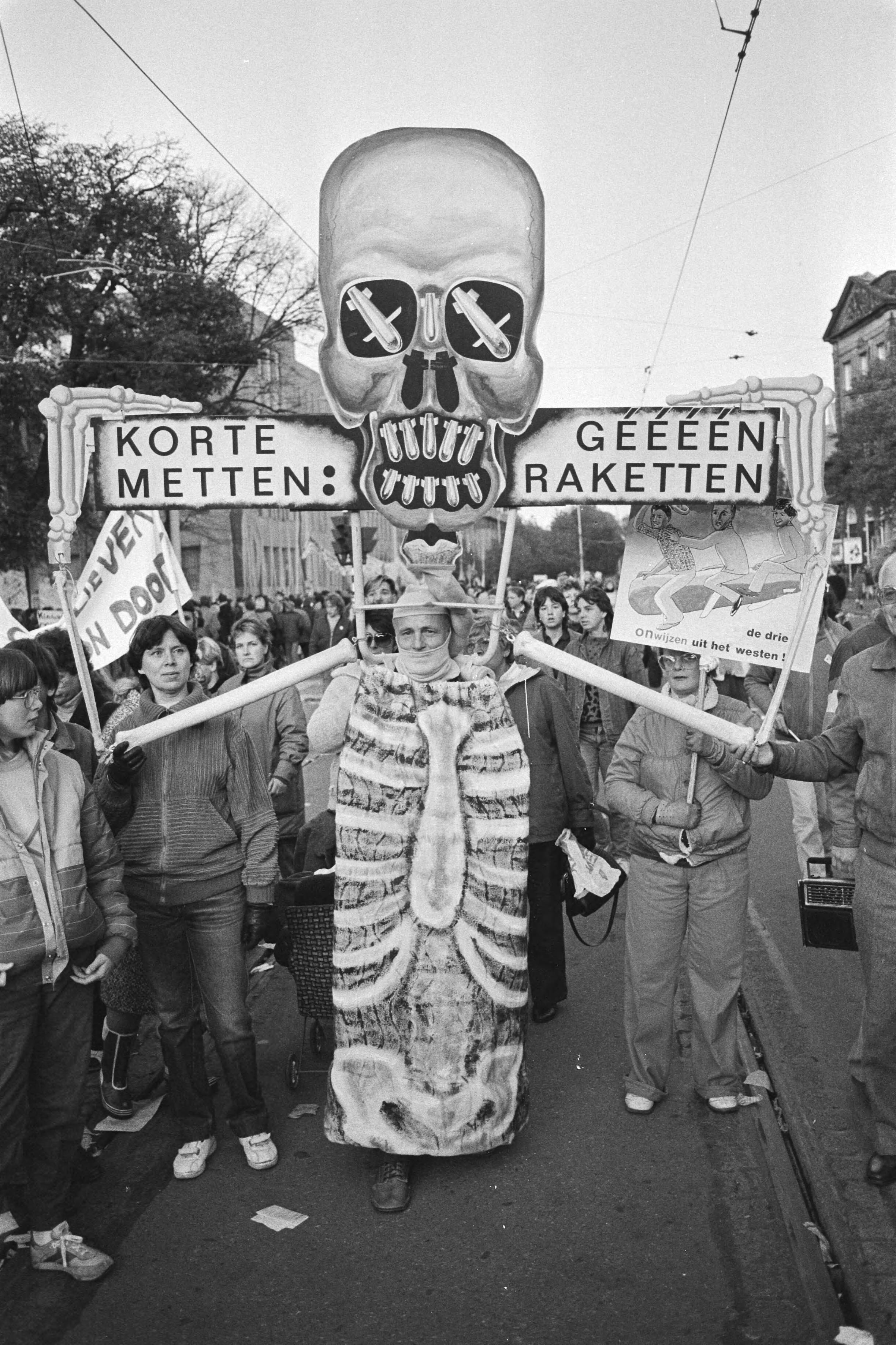 Vredesdemonstratie Den Haag , 550.000 mensen demonstreren o.m. tegen plaatsing kruisrakette — Demonstrant verkleed als groot skelet met het opschrift "Korte metten: géééén raketten" — Foto: Antonisse, Marcel / Anefo. Licentie: Set B: Rechtenvrij / Publiek Domein. Bron: Nationaal Archief. http://hdl.handle.net/10648/ad2fe184-d0b4-102d-bcf8-003048976d84