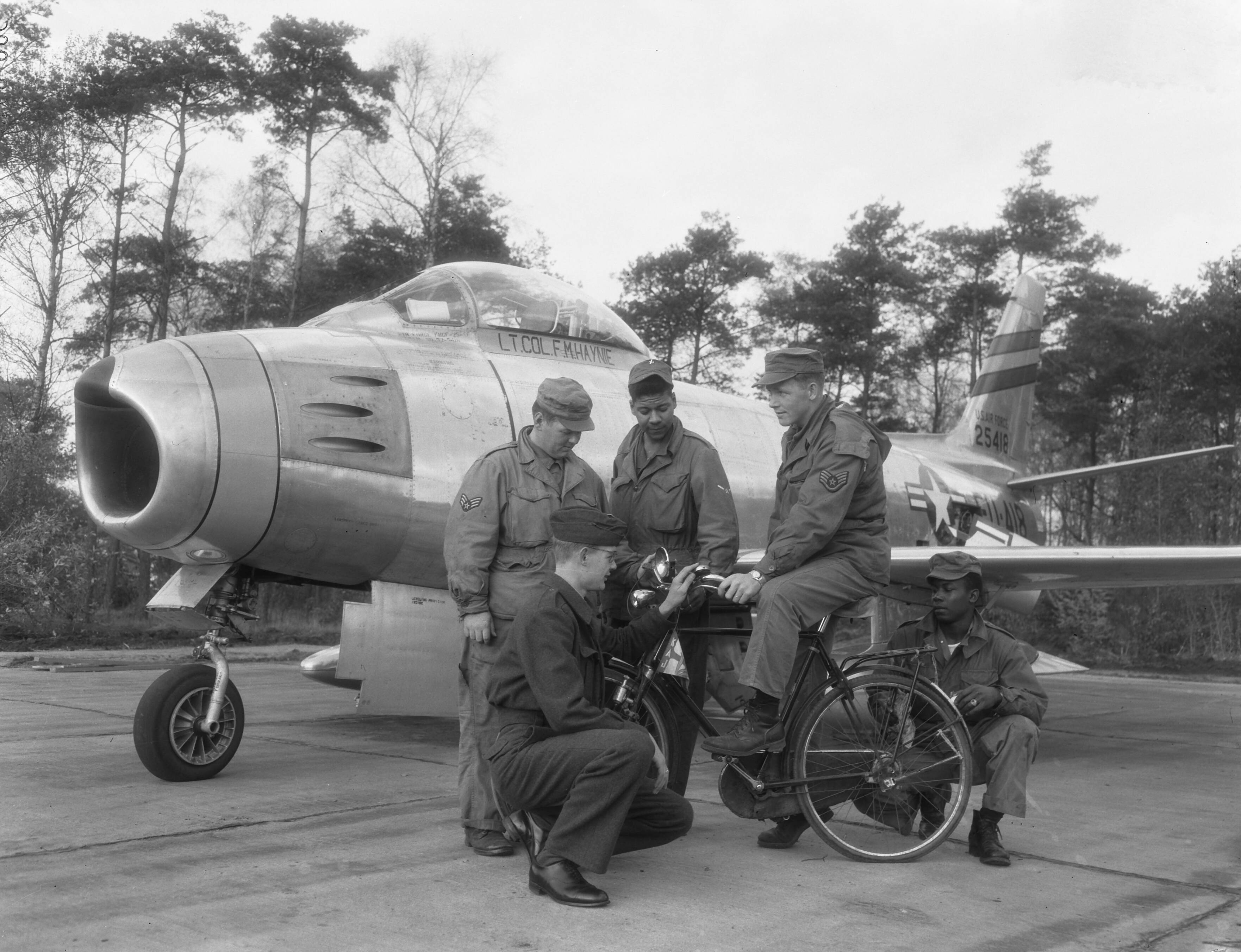 Fotocollectie Anefo — [North American F-86 Sabres van het USAF 32th Fighter Day Squadron gestationeerd op Soesterberg] Nederlandse luchtmachtmilitair met fiets en Amerikanen — Foto: Duinen, G.W. van / Anefo. Licentie: Set B: Rechtenvrij / Publiek Domein. Bron: Nationaal Archief. http://hdl.handle.net/10648/a92cb0c6-d0b4-102d-bcf8-003048976d84