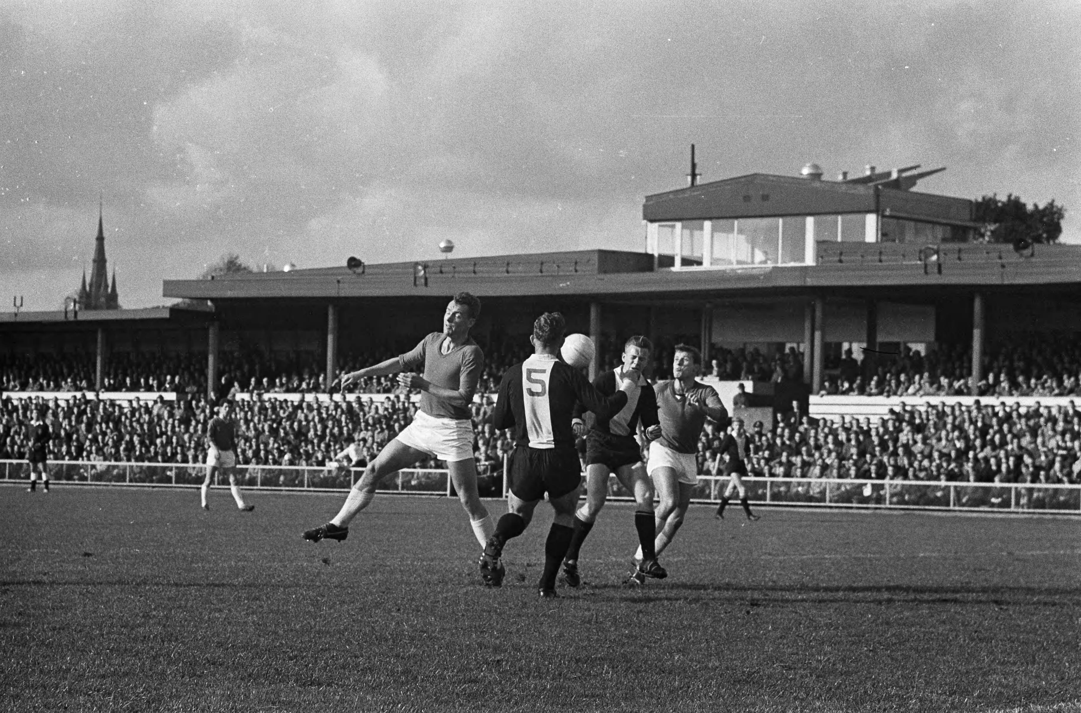 Fotocollectie Anefo — Voetbal. 't Gooi tegen Alkmaar '54 1-1. Spelmoment, De Vries (Alkmaar), van de Eshof ('t Gooi), van der Straten ('t Gooi) en Hanek (Alkmaar) — Foto: Gelderen, Hugo van / Anefo. Licentie: Set B: Rechtenvrij / Publiek Domein. Bron: Nationaal Archief. http://hdl.handle.net/10648/aa49516c-d0b4-102d-bcf8-003048976d84