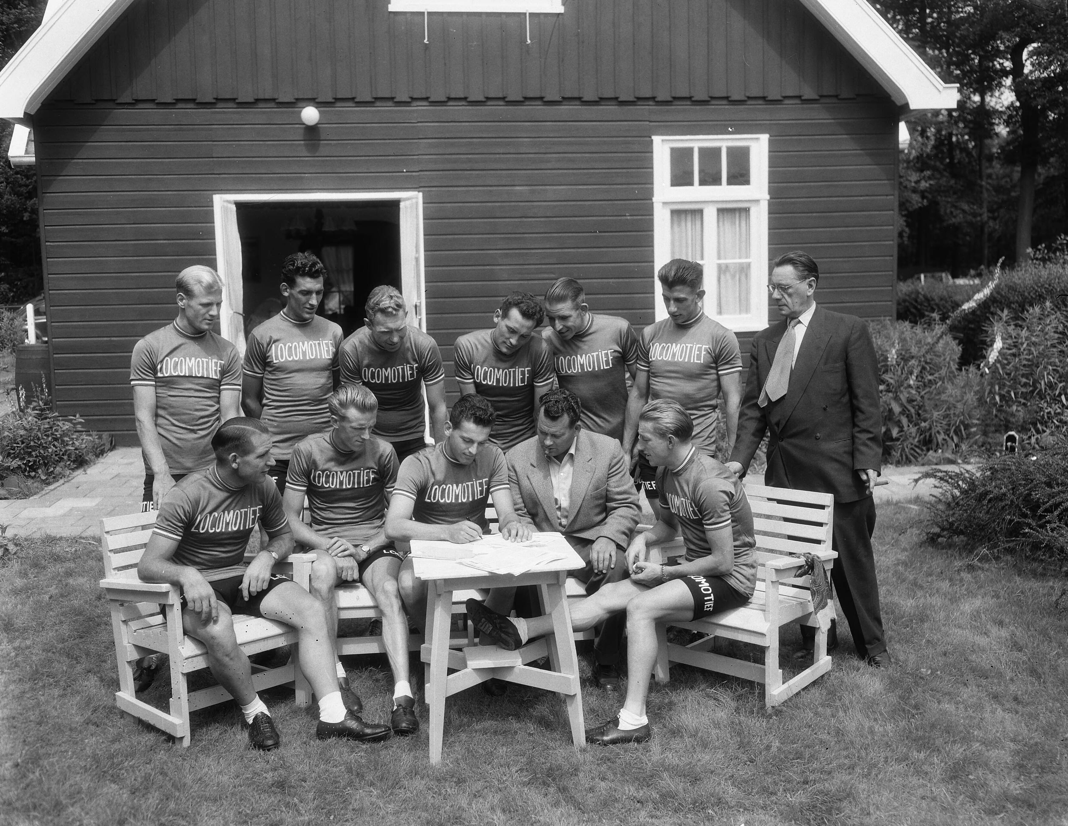 Ondertekening van contracten van Tour de France ploeg ten huize van Cees Pellenaars te Breda — Ondertekening van contracten van Tour de France ploeg ten huize van Cees Pellenaars te Breda, groep [staand vlnr. Adri Suijkerbuijk, Gerrit Voorting, Henk Faanhof, Hein van Breenen, Nico van Est, Thijs Roks, ?, Zittend vlnr. Wim van Est, Jan Nolten, Jules Maenen, Cees Pellenaars en Wout Wagtmans — Foto: Duinen, G.W. van / Anefo. Licentie: Set B: Rechtenvrij / Publiek Domein. Bron: Nationaal Archief. http://hdl.handle.net/10648/a924ab7e-d0b4-102d-bcf8-003048976d84