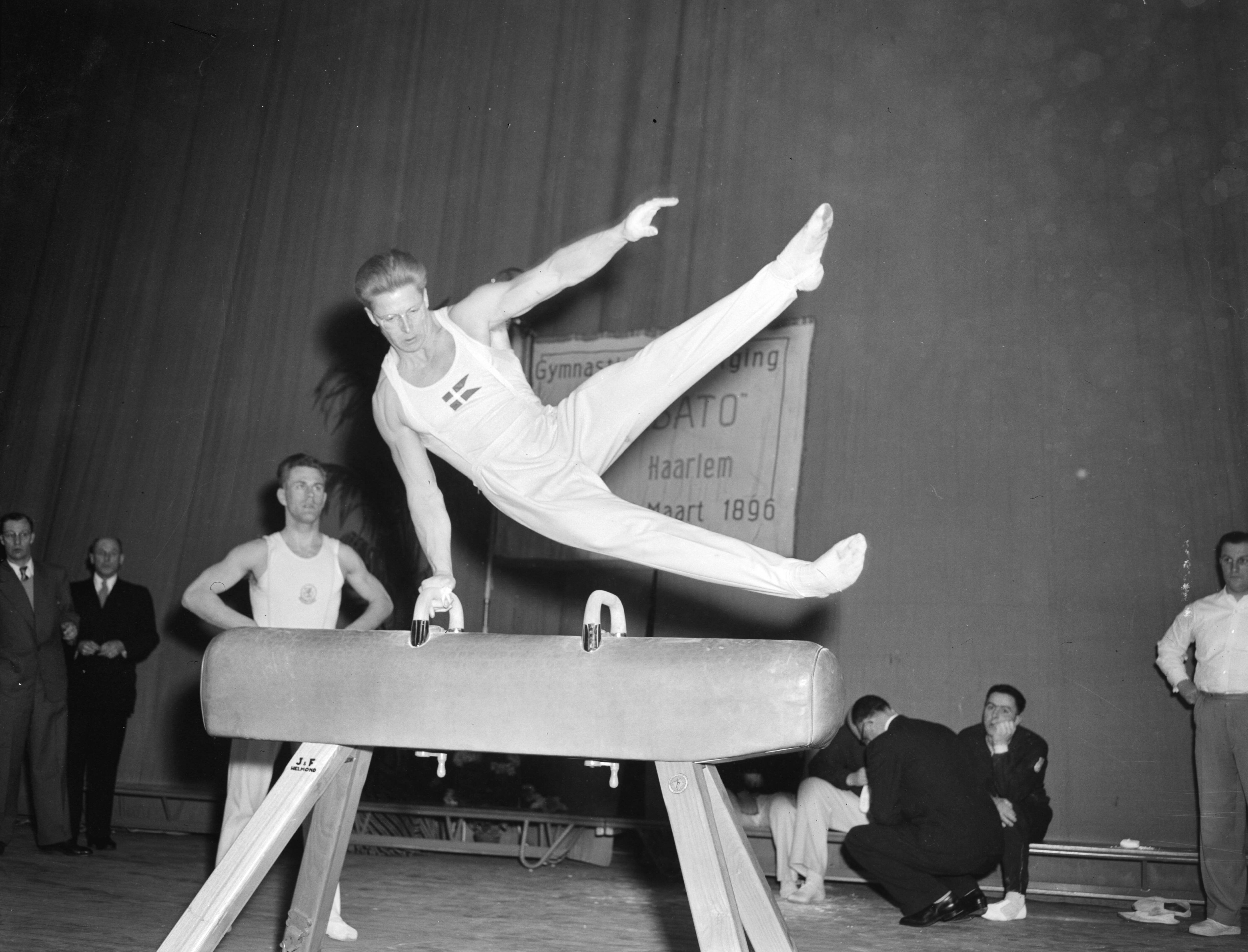 Fotocollectie Anefo — Turnen. Landenwedstrijd Nederland tegen Denemarken te Haarlem. Elkana Grønne (Denemarken) in actie bij paardvoltige. Klaas Boot kijkt toe — Foto: Fotograaf Onbekend / Anefo. Licentie: Set B: Rechtenvrij / Publiek Domein. Bron: Nationaal Archief. http://hdl.handle.net/10648/afd13564-d0b4-102d-bcf8-003048976d84