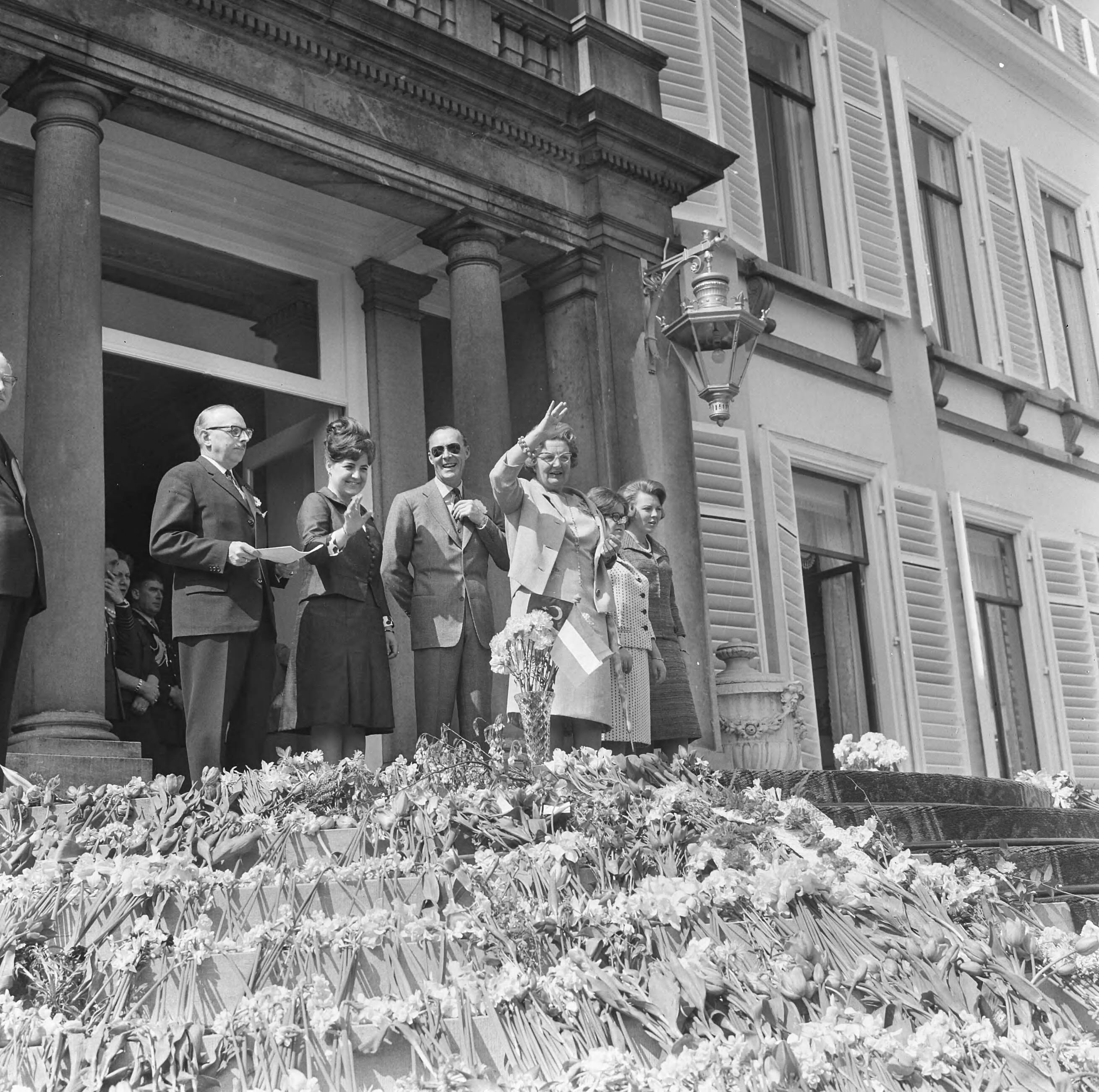 Koninginnedag 1965 — De koninklijke familie wuift van het bordes naar het langstrekkende defilé, prinses Margriet, prins Bernhard, koningin Juliana, prinses Christina en prinses Beatrix — Foto: Koch, Eric / Anefo. Licentie: Set B: Rechtenvrij / Publiek Domein. Bron: Nationaal Archief. http://hdl.handle.net/10648/aaa4139a-d0b4-102d-bcf8-003048976d84