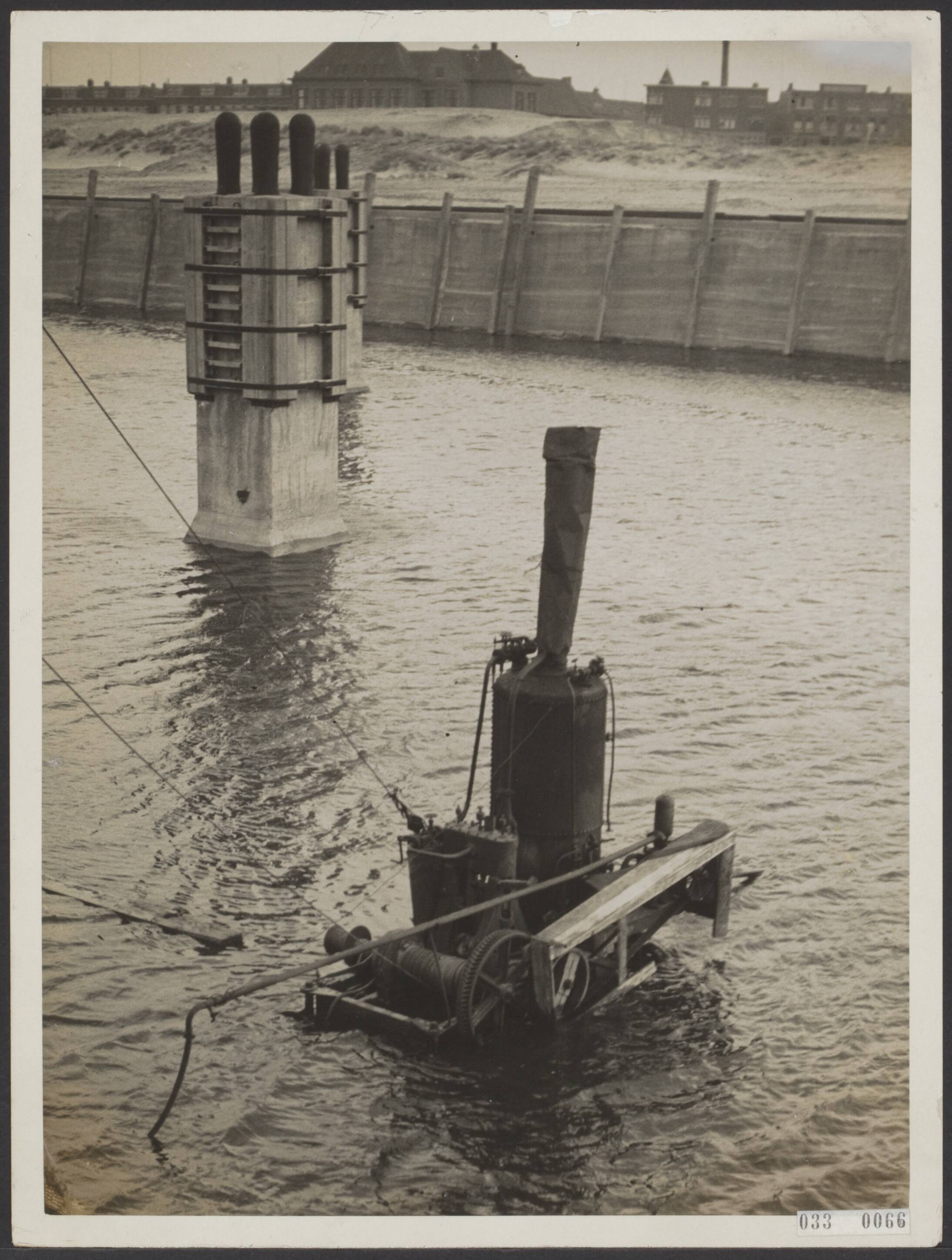 Fotocollectie Elsevier Binnenland — Ten gevolge van de grote druk van het water in het verbindingskanaal bezweek de afsluitdam van de nieuwe vissershaven van Scheveningen, waardoor deze haven ontijdig met water werd gevuld. Een heimachine die de allures van een dukdalf heeft aangenomen — Foto: N.V. Polygoon. Licentie: Set B: Rechtenvrij / Publiek Domein. Bron: Nationaal Archief. http://hdl.handle.net/10648/ade5c710-d0b4-102d-bcf8-003048976d84