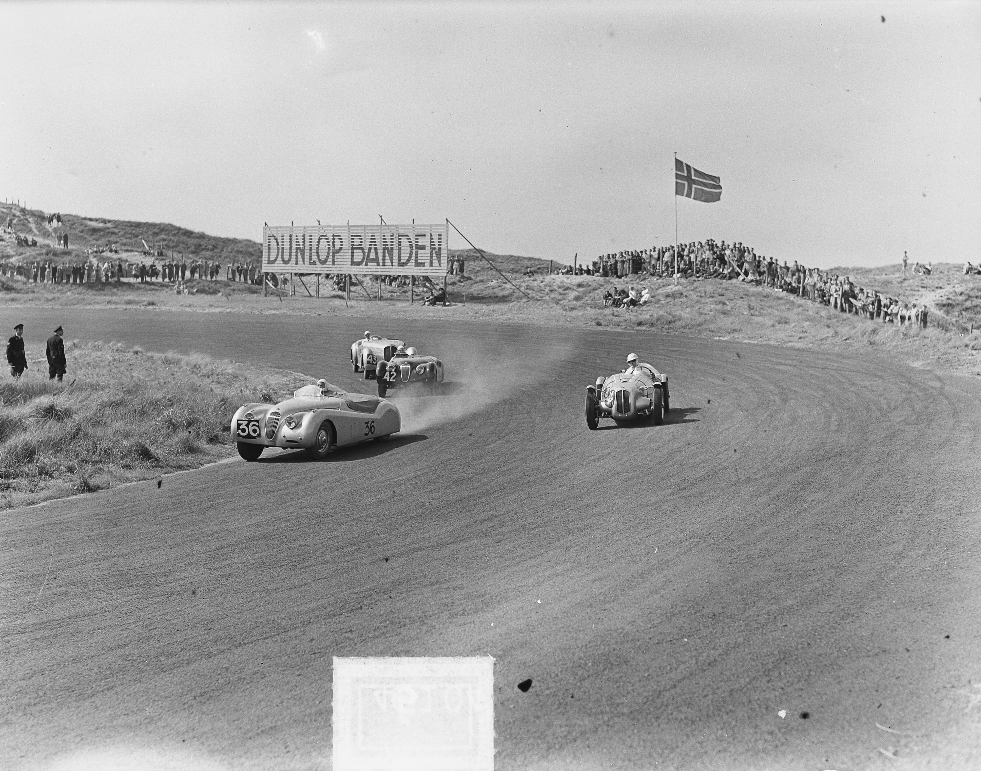 Motor- en autoraces KNAC en KNMV op het circuit van Zandvoort — Motor- en autoraces van KNAC en KNMV op het circuit van Zandvoort [klasse boven 2000cc in de Tarzanbocht. Voorop winnaar dr. Oei Tjong Bo met zijn Jaguar (nr. 36). Daarachter met nr. 42 Van Dieten, ook met een Jaguar en no 43, Tielens met een Delahaye] — Foto: Pot, Harry / Anefo. Licentie: Set B: Rechtenvrij / Publiek Domein. Bron: Nationaal Archief. http://hdl.handle.net/10648/a8eb4bd6-d0b4-102d-bcf8-003048976d84