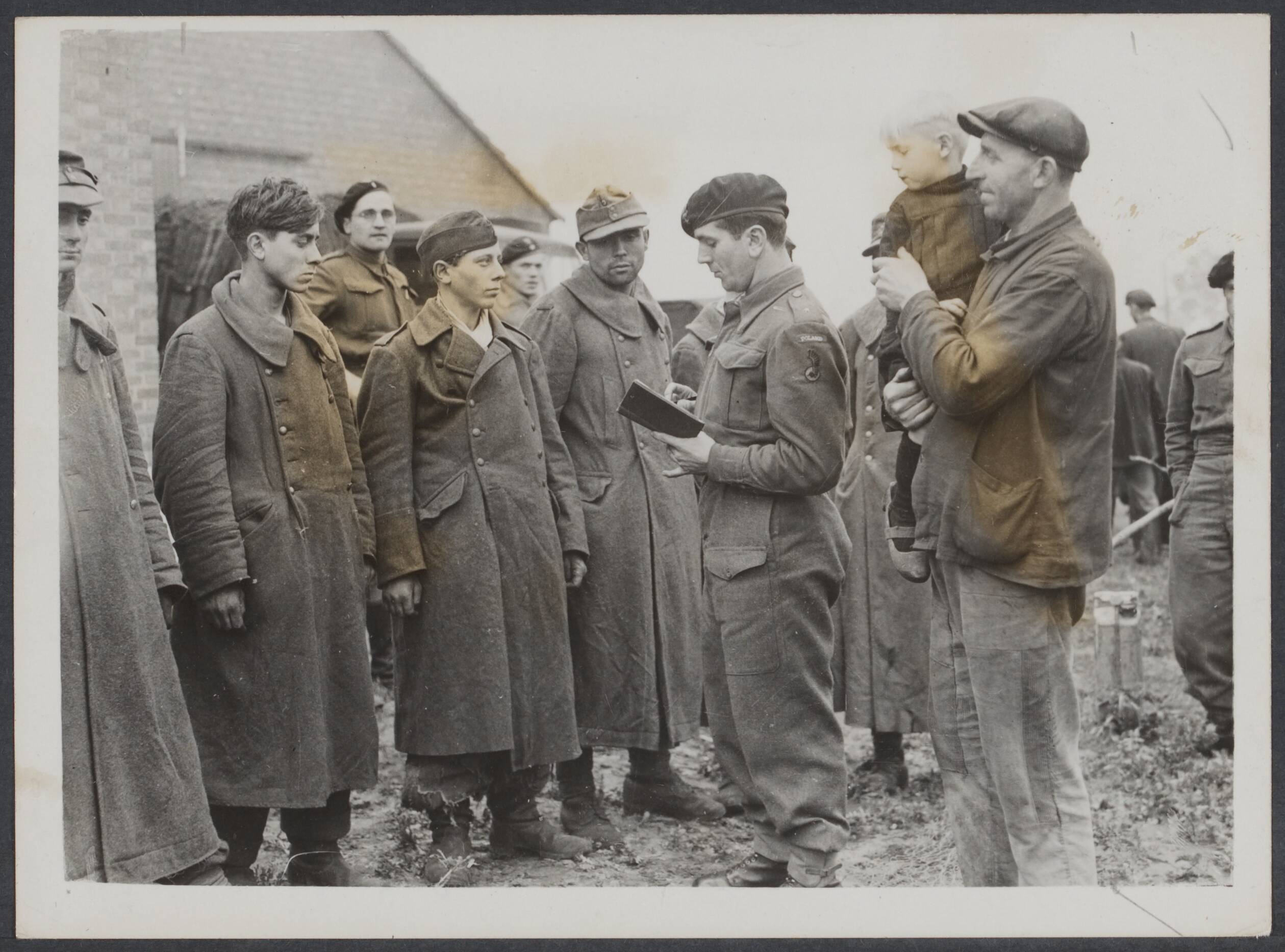 Nederland front, 1944 — Poolse leger aan het front Breda-Tilburg. Na de verovering van Alphen en Gilze. Duitse krijgsgevangenen worden geregistreerd door een Poolse militair terwijl een boer met zijn zoontje op de arm toekijkkt — Foto: Keystone / Rechtenvrij. Licentie: Set B: Rechtenvrij / Publiek Domein. Bron: Nationaal Archief. http://hdl.handle.net/10648/6f3a8f4f-d6c5-a86a-af4c-35cc69671d0c