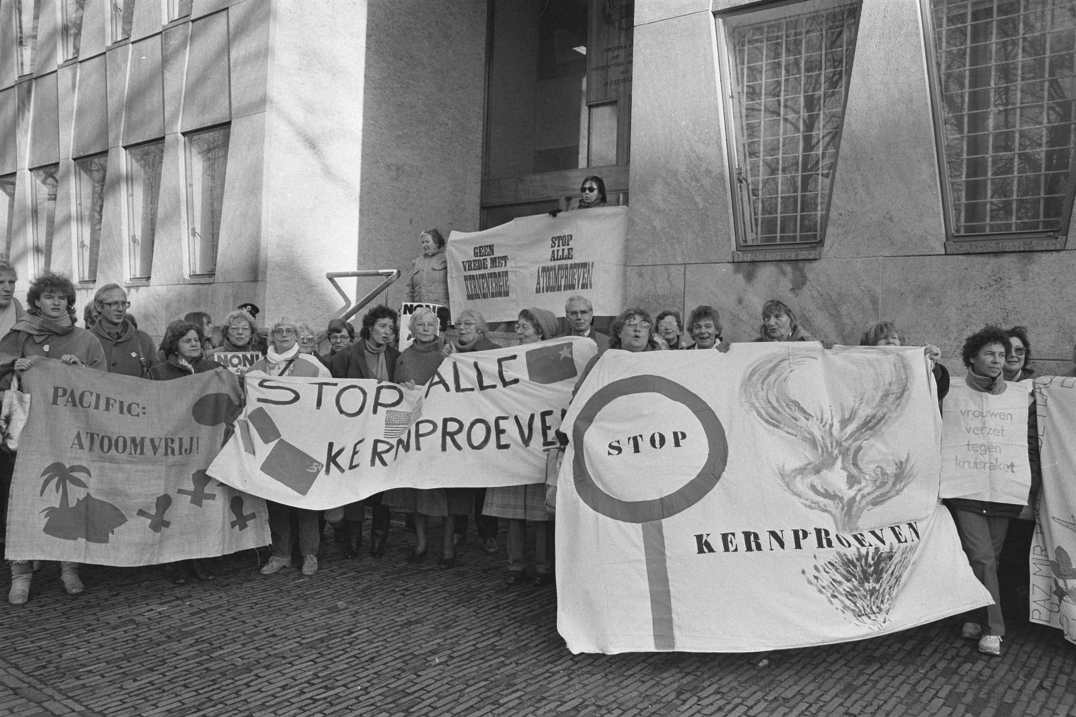 Fotocollectie Anefo — Vrouwenprotest tegen atoomproeven bij Amerikaanse ambassade in Den Haag — Foto: Gerrits, Roland / Anefo. Licentie: Set B: Rechtenvrij / Publiek Domein. Bron: Nationaal Archief. http://hdl.handle.net/10648/ad5a79a8-d0b4-102d-bcf8-003048976d84