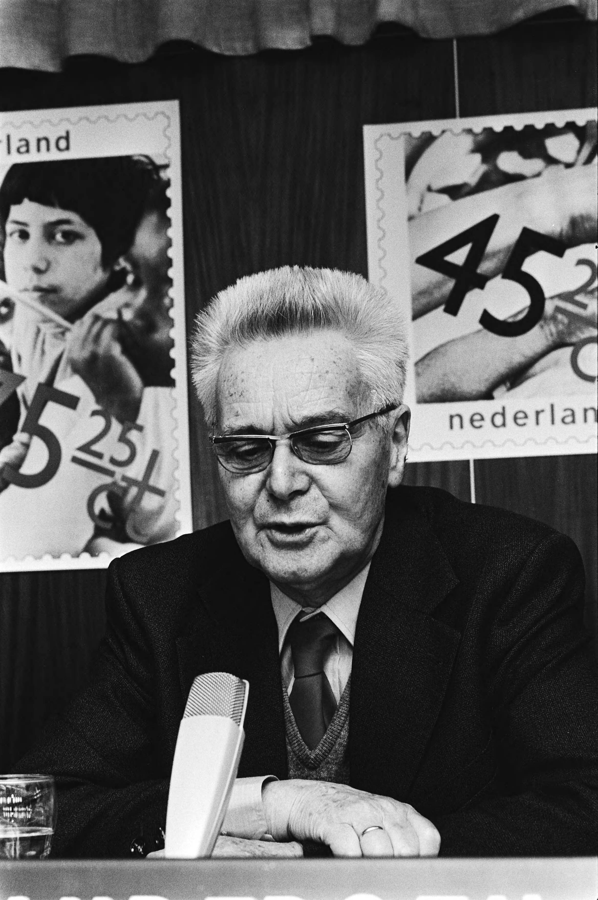 Symposium in Den Haag t.g.v. uitbrengen kinderpostzegel overzicht tafel — Prof. dr. Jan Tinbergen achter de microfoon — Foto: Suyk, Koen / Anefo. Licentie: Set B: Rechtenvrij / Publiek Domein. Bron: Nationaal Archief. http://hdl.handle.net/10648/acd4b084-d0b4-102d-bcf8-003048976d84