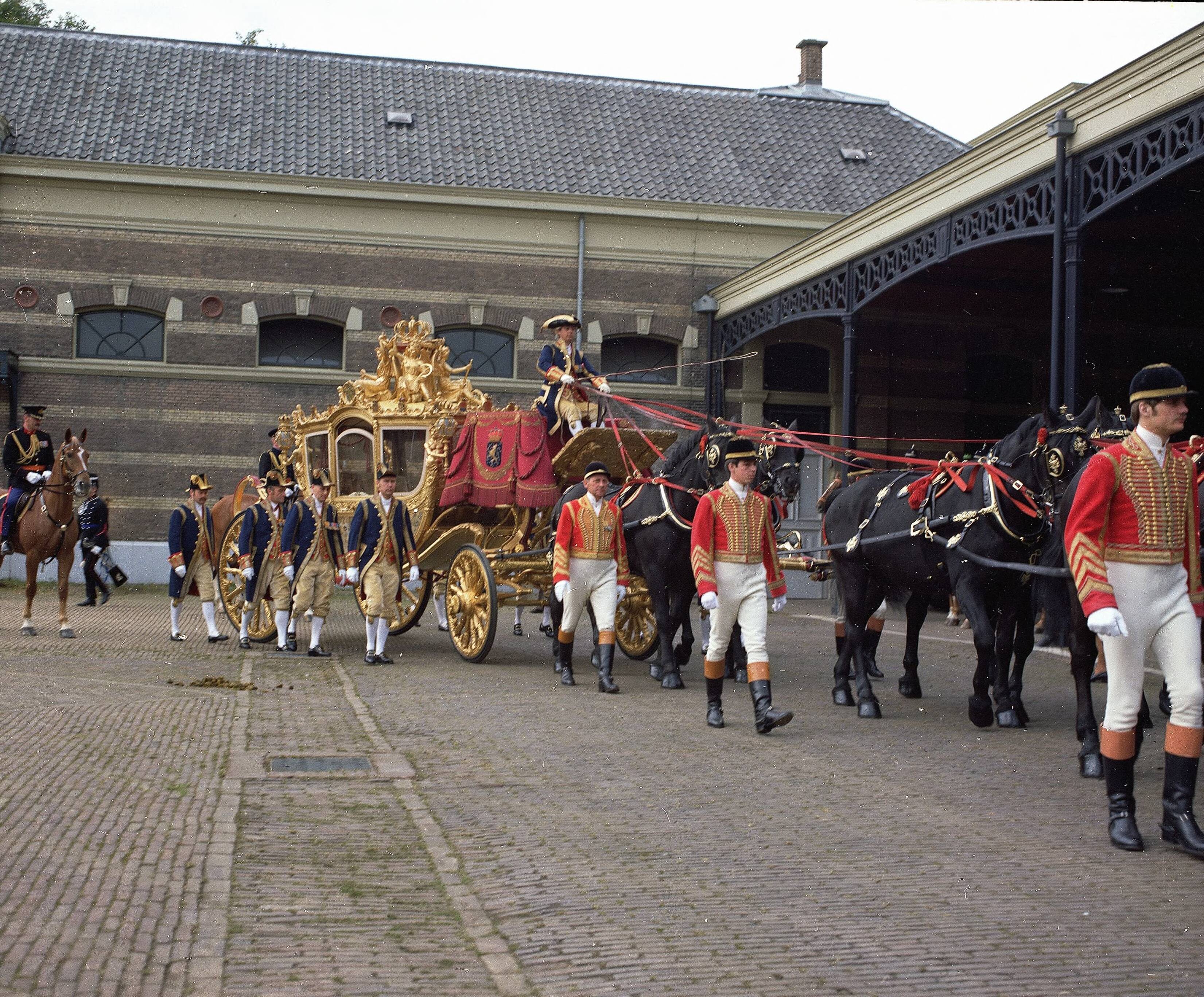 Fotocollectie RVD / Koninklijk Huis — Gouden koets met koetsier, stalpersoneel, lakeien en paarden op de binnenplaats van de koninklijke stallen aan de Noordwal in Den Haag — Foto: Mastenbroek, Cees / RVD. Licentie: Set B: Rechtenvrij / Publiek Domein. Bron: Nationaal Archief. http://hdl.handle.net/10648/afb27714-d0b4-102d-bcf8-003048976d84