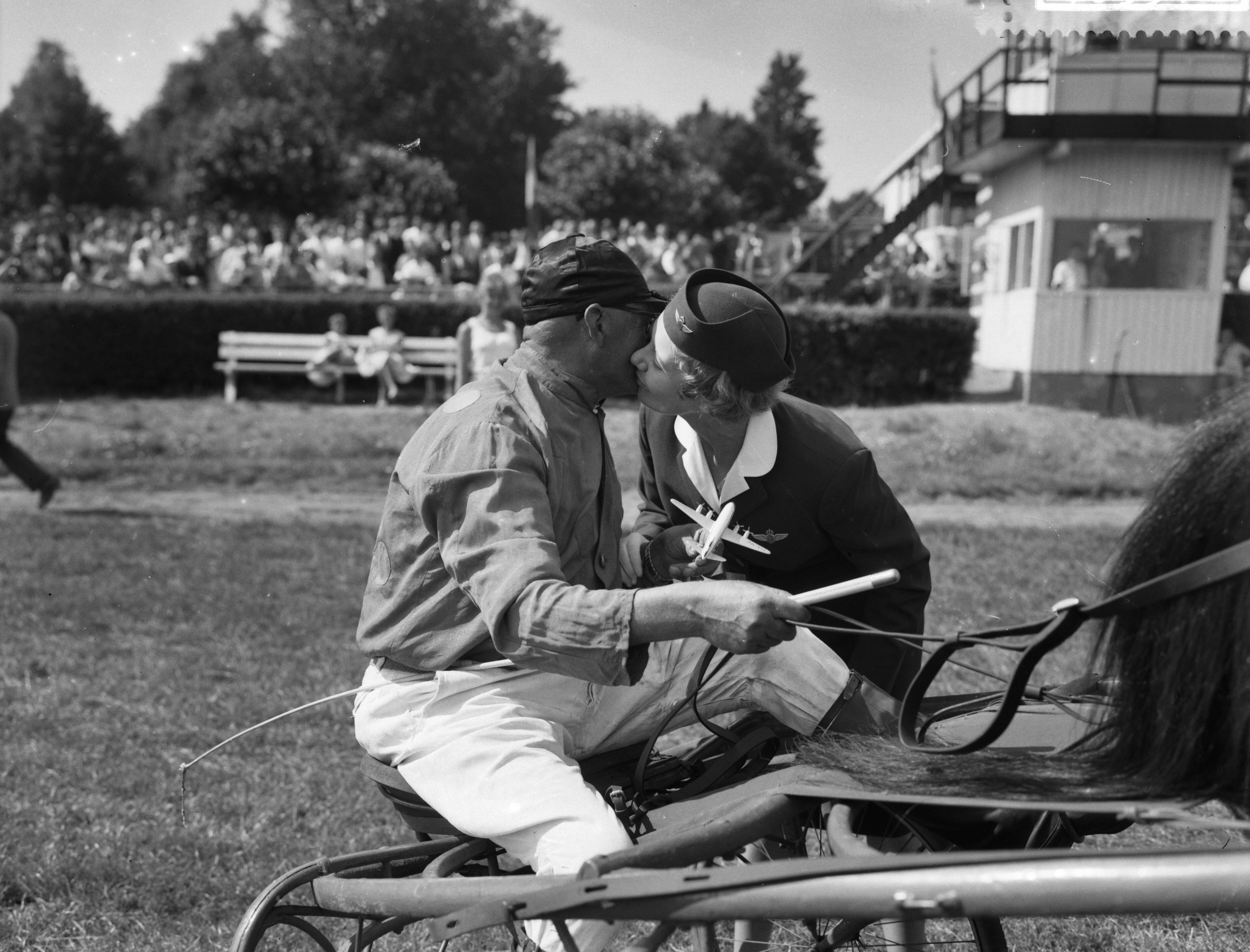 Fotocollectie Anefo — Draverijen gewijd aan de KLM op Duindigt, mr. T. Hames stewardess bij de KLM feliciteert de pikeur J. P. de Vlieger, die drie draverijen won — Foto: Rossem, Wim van / Anefo. Licentie: Set B: Rechtenvrij / Publiek Domein. Bron: Nationaal Archief. http://hdl.handle.net/10648/a999bc66-d0b4-102d-bcf8-003048976d84