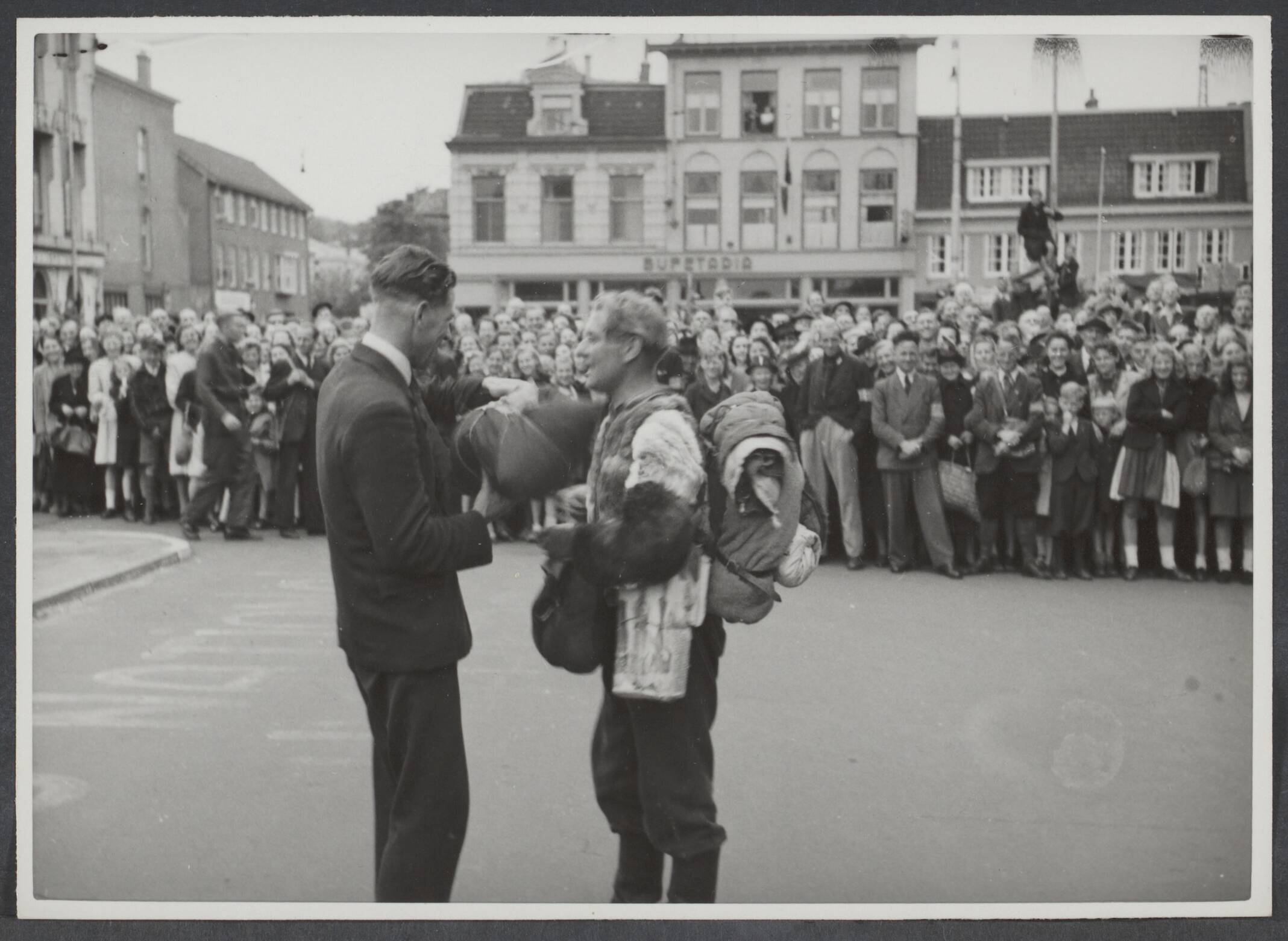 Arbeidsdienst. Waaronder "Nederlandse Arbeidsdienst" en "Vreugde en Arbeid" ("Fut door lol" 81). Ook opbouwdienst 1940/41. — [Serie: repatriëring Arbeitseinsatz] Juni-Juli 1945. [een repatriant met bepakking krijgt iets uitgeriek, om hem heen veel publiek] — Foto: Bosen, Frans / Spaarnestad. Licentie: Set B: Rechtenvrij / Publiek Domein. Bron: Nationaal Archief. http://hdl.handle.net/10648/39170d3a-5d57-7f5a-bc33-6e00d2650551