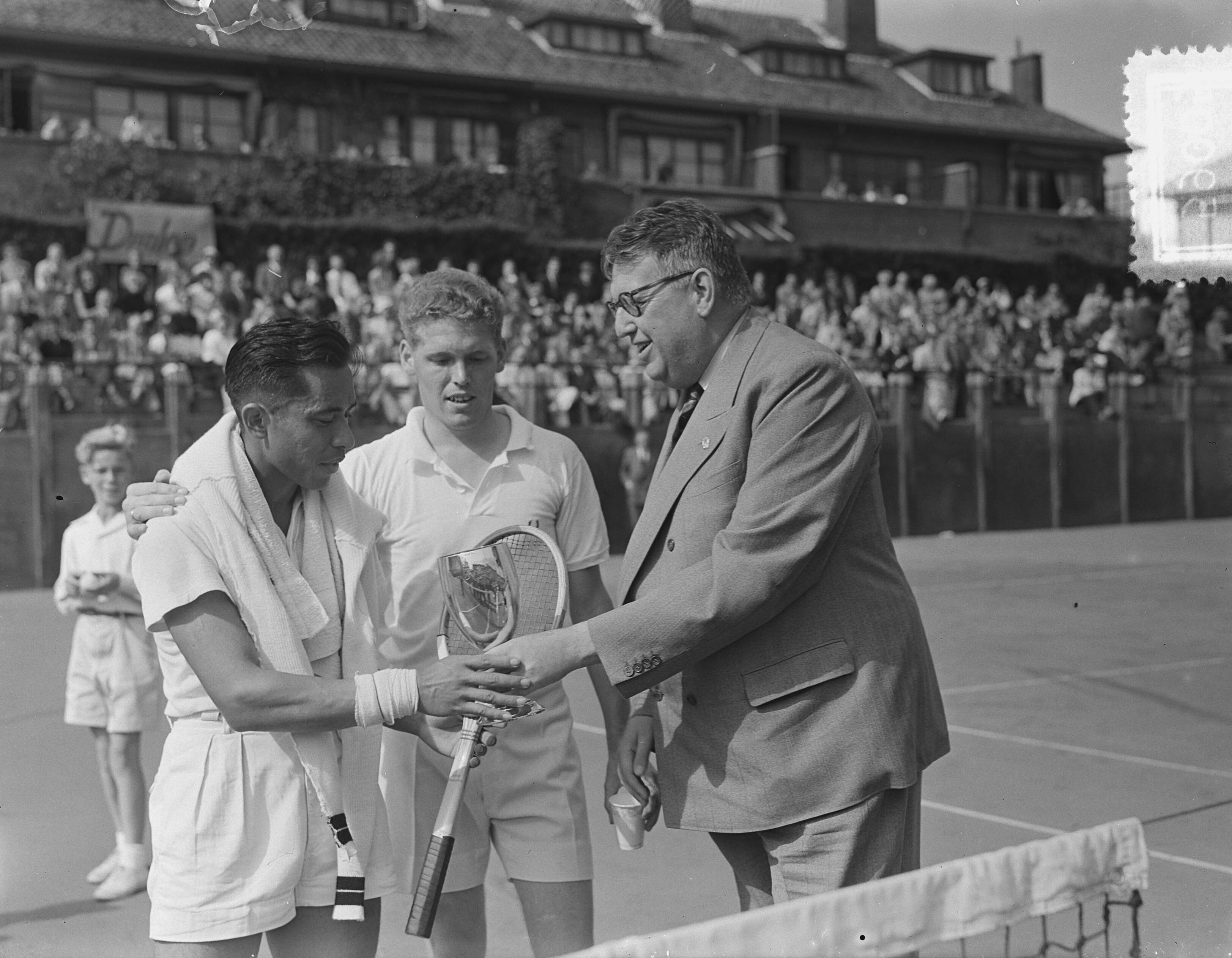 Tenniskampioenschappen Scheveningen — Tenniskampioenschappen Scheveningen. Lex Karamoy (links) won de titel in het enkelspel en ontvangt de beker uit handen van de vice-voorzitter van de K.N.L.B. mr. F. Meyer In het midden Fred Dehnert, zijn tegenstander in de finale — Foto: Bilsen, Joop van / Anefo. Licentie: Set B: Rechtenvrij / Publiek Domein. Bron: Nationaal Archief. http://hdl.handle.net/10648/a91198cc-d0b4-102d-bcf8-003048976d84