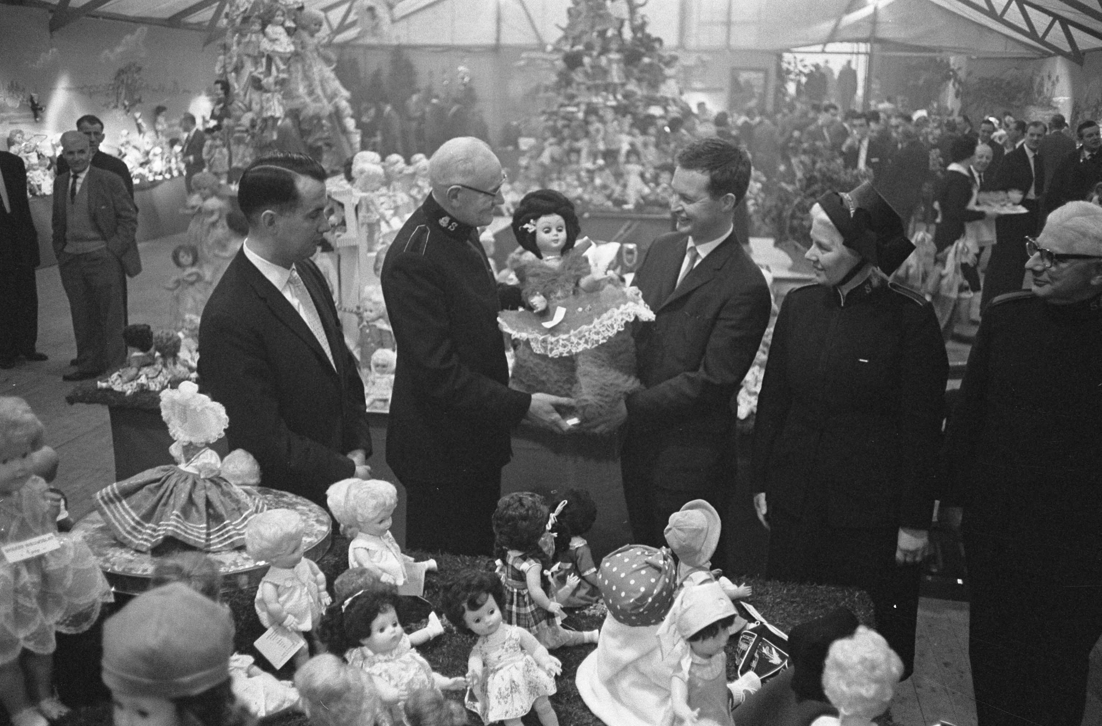 Fotocollectie Anefo — Albert Heijn N.V. in Zaandam heeft t.g.v. het 75-jarig bestaan aan haar vrienden en relaties gevraagd poppen te schenken i.p.v. de gebruikelijke cadeaus. Tijdens een receptie in Zaandam heeft de directie de poppen aan het Leger des Heils aangeboden. Links directeur J. Heijn, en rechts president-directeur A. Heijn die een pop overhandigt aan de landelijk commandant, W.F. Palstra — Foto: Pot, Harry / Anefo. Licentie: Set B: Rechtenvrij / Publiek Domein. Bron: Nationaal Archief. http://hdl.handle.net/10648/aa0a2410-d0b4-102d-bcf8-003048976d84