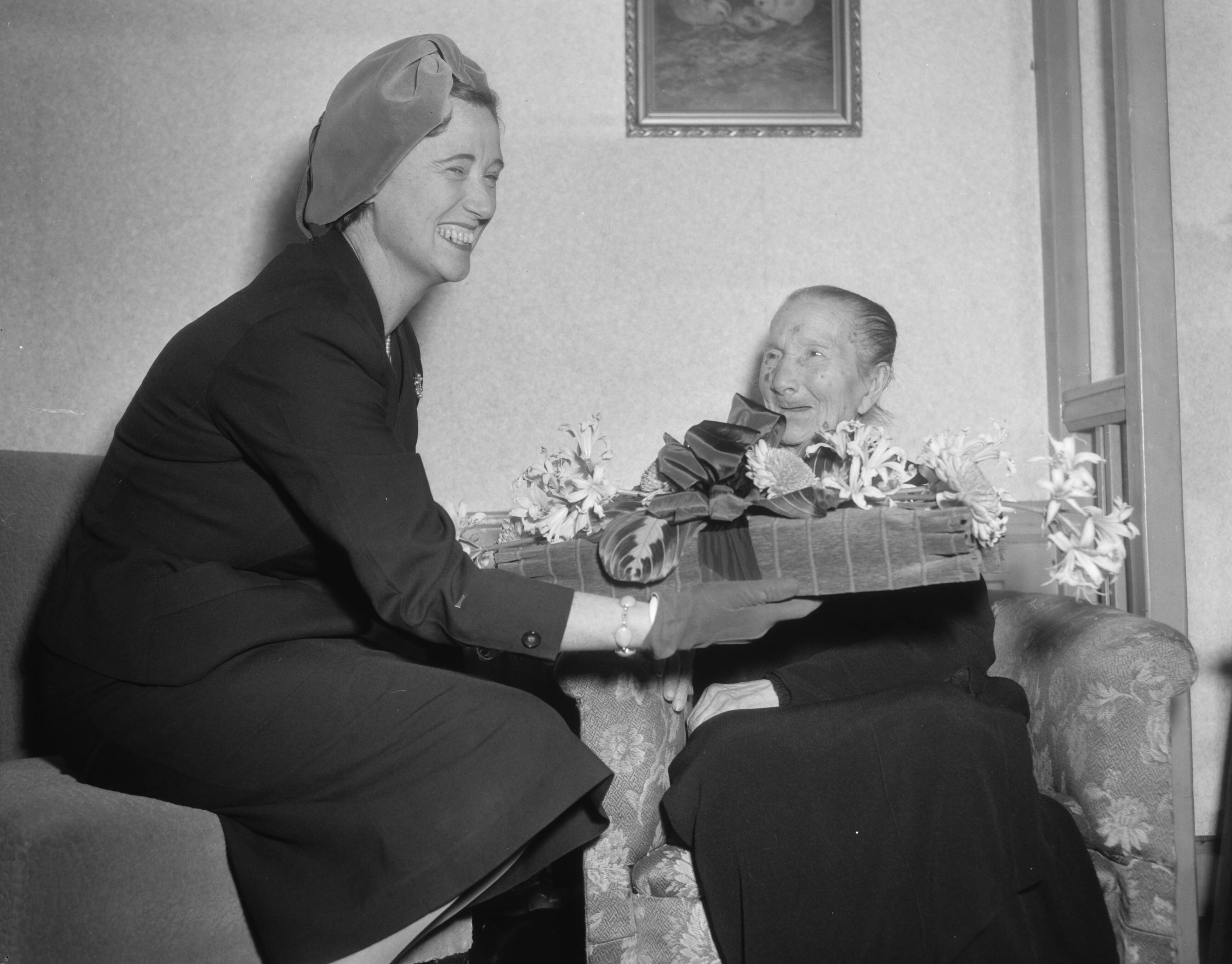 Fotocollectie Anefo — Oudste inwoonster van Den Haag, mevrouw J.J. de Calonne-Meister wordt 108 jaar en wordt gefeliciteerd door mevr. Kolfschoten, de echtgenote van de burgemeester van Den Haag — Foto: Pot, Harry / Anefo. Licentie: Set B: Rechtenvrij / Publiek Domein. Bron: Nationaal Archief. http://hdl.handle.net/10648/a96e4cf2-d0b4-102d-bcf8-003048976d84