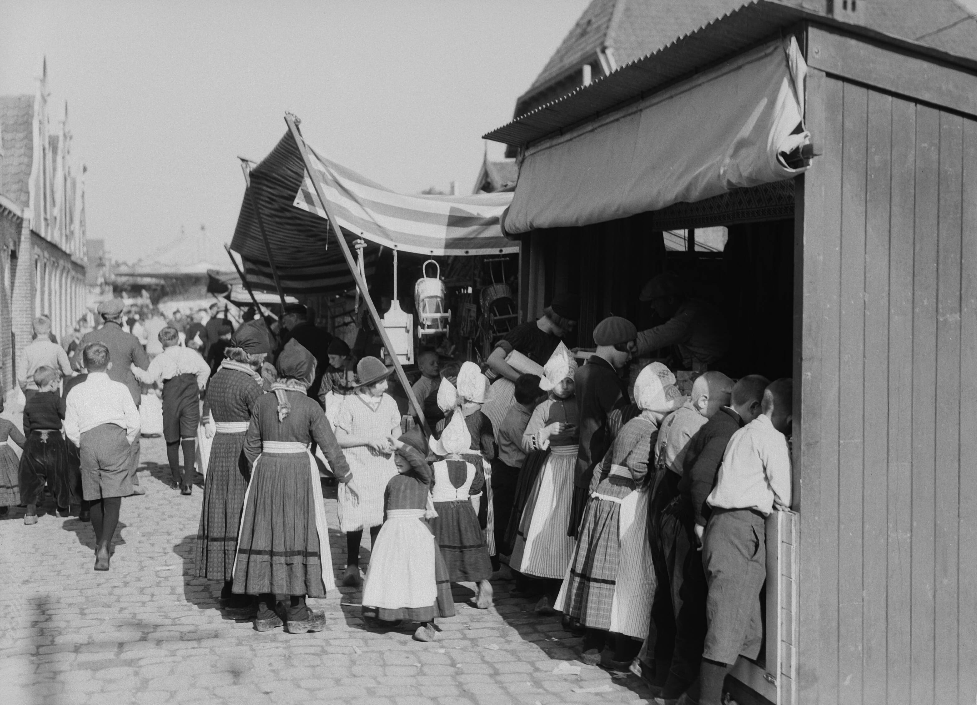 Klederdrachten in Nederland — Kinderen in klederdracht in Volendam bij een marktkraam — Foto: Poll, Willem van de. Licentie: Set B: Rechtenvrij / Publiek Domein. Bron: Nationaal Archief. http://hdl.handle.net/10648/aea05b20-d0b4-102d-bcf8-003048976d84