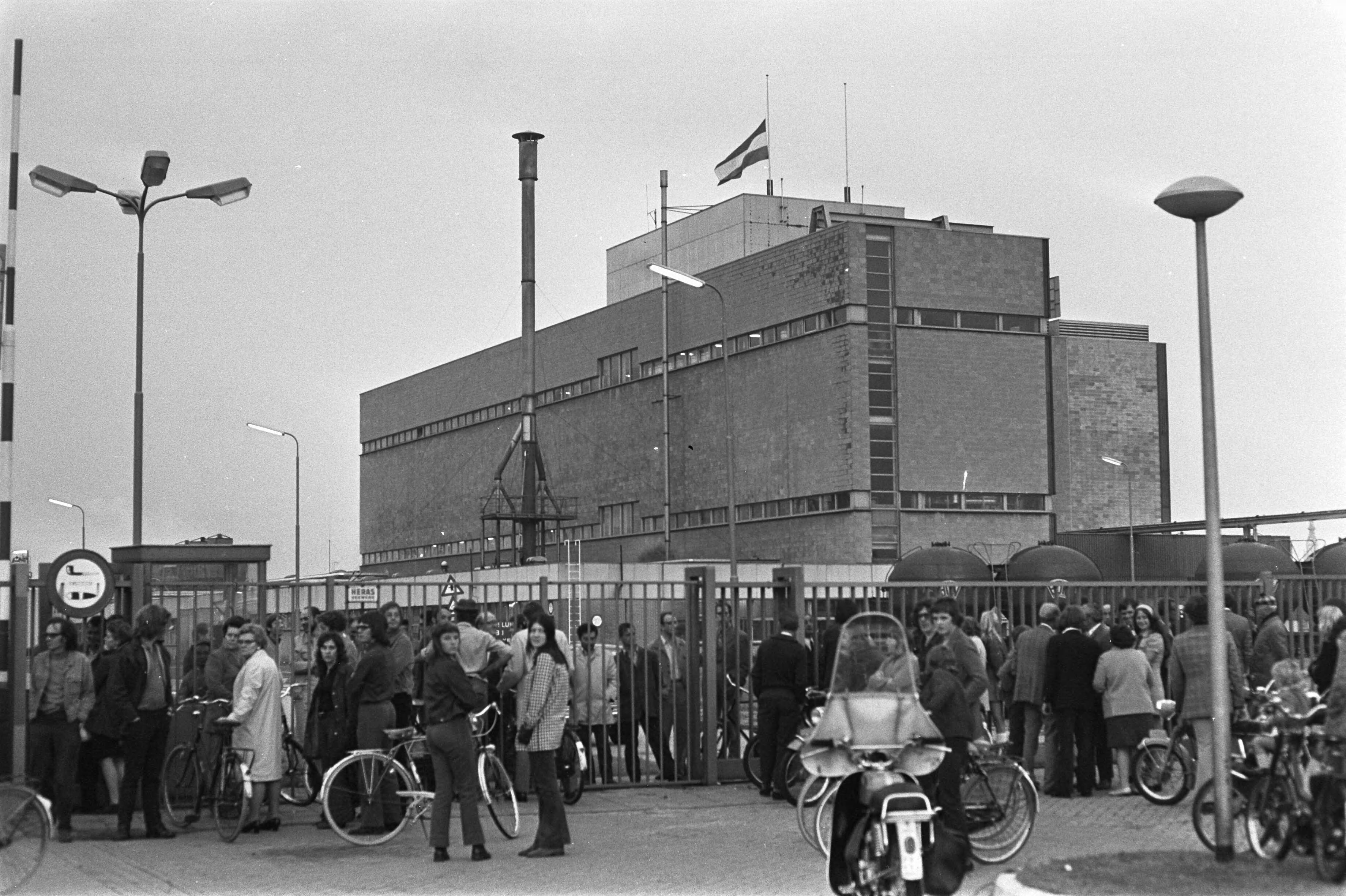 Fotocollectie Anefo — ENKA-bedrijf te Breda bezet door werknemers, arbeiders bi gesloten hek met op achtergrond het bedrijf met de vlag halfstok — Foto: Peters, Hans / Anefo. Licentie: Set B: Rechtenvrij / Publiek Domein. Bron: Nationaal Archief. http://hdl.handle.net/10648/abf64196-d0b4-102d-bcf8-003048976d84