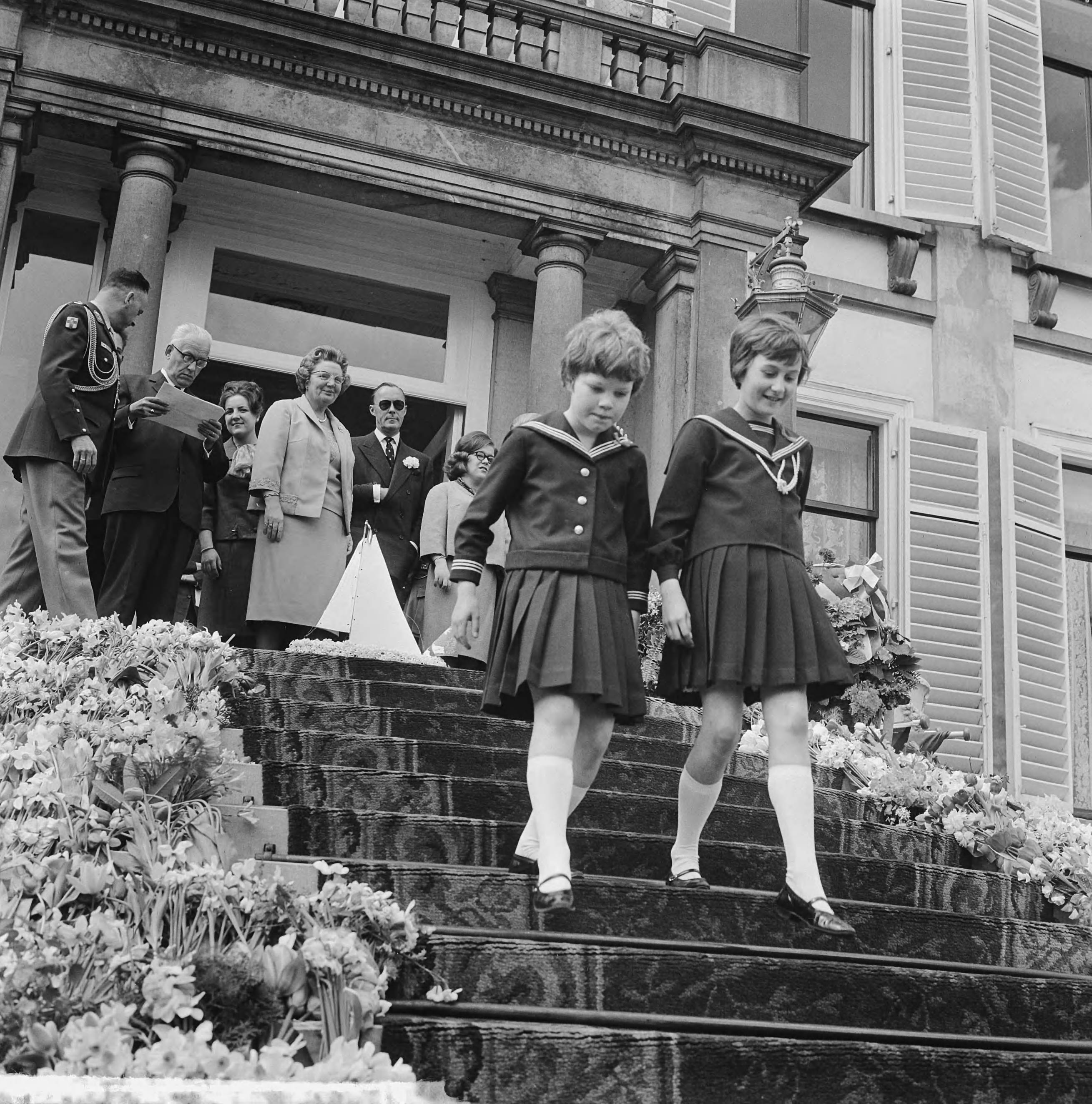 Koninginnedag 1964 — Defilé Soestdijk, koninklijke familie op bordes, twee meisje dalen de trappen af — Foto: Nijs, Jac. de / Anefo. Licentie: Set B: Rechtenvrij / Publiek Domein. Bron: Nationaal Archief. http://hdl.handle.net/10648/aa66efa6-d0b4-102d-bcf8-003048976d84