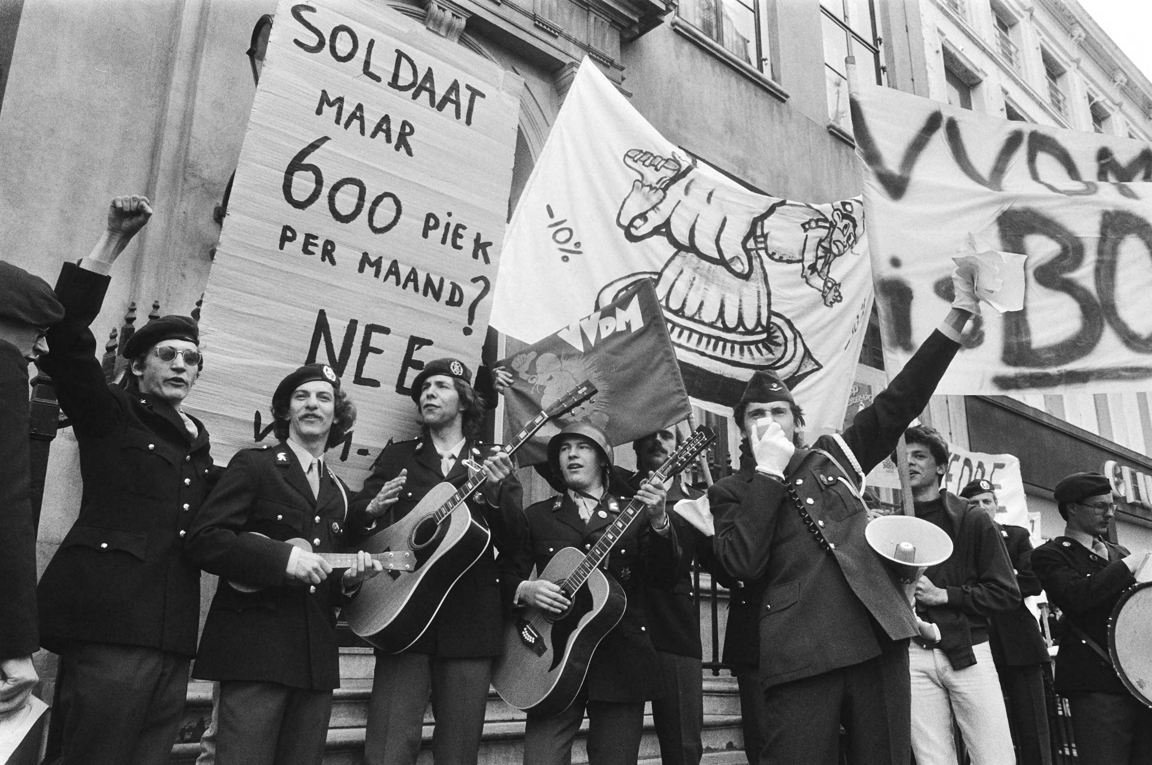 Protest van dienstplichtige militairen tegen weddeverlaging in Den Haag — Dienstplichtigen met muziekinstrumenten en spandoeken — Foto: Bogaerts, Rob / Anefo. Licentie: Set B: Rechtenvrij / Publiek Domein. Bron: Nationaal Archief. http://hdl.handle.net/10648/ad289a82-d0b4-102d-bcf8-003048976d84
