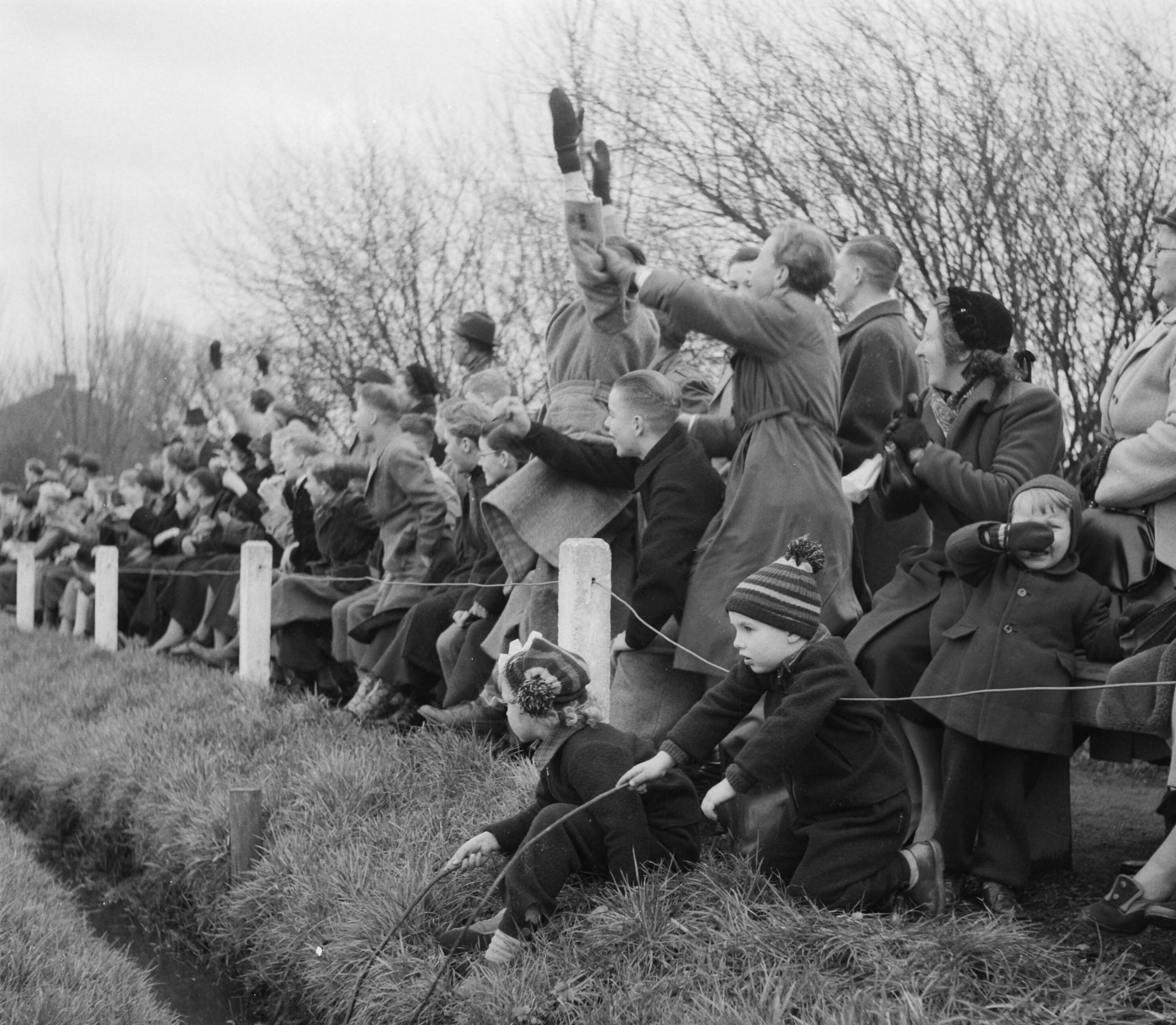 Fotocollectie Anefo — Korfbal. Koog Zaandijk tegen Westerkwartier 4-7. Supporters langs het veld juichen. In de voorgrond twee kinderen die "vissen" in een greppel. Een kind rechts huilt — Foto: Noske, J.D. / Anefo. Licentie: Set B: Rechtenvrij / Publiek Domein. Bron: Nationaal Archief. http://hdl.handle.net/10648/a8f42b02-d0b4-102d-bcf8-003048976d84
