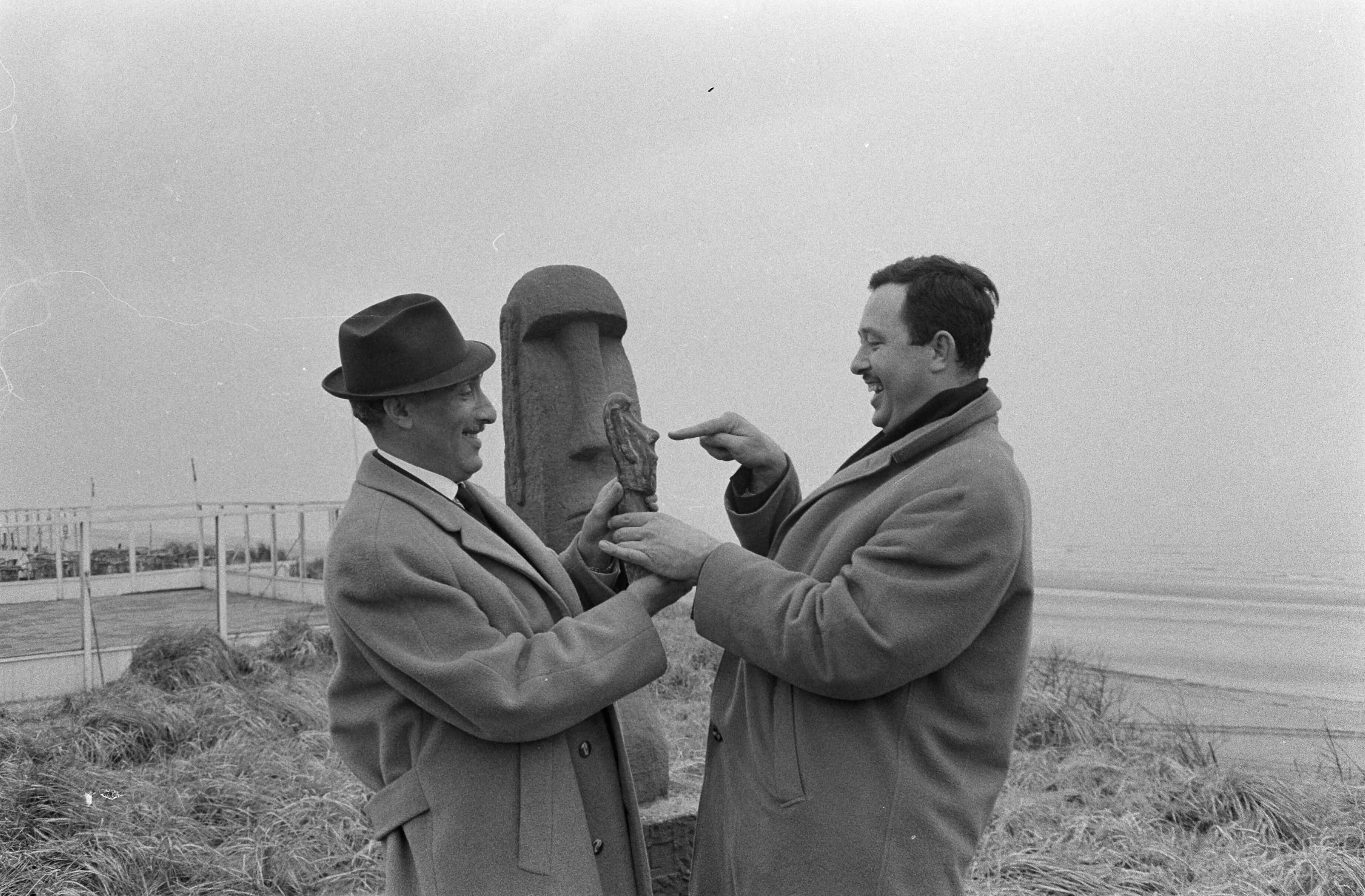 Fotocollectie Anefo — Nederland krijgt een „grapjas”-prijs, die jaarlijks op 1 april in Zandvoort zal worden uitgereikt voor de best geslaagde grap van het afgelopen jaar. De prijs bestaat uit een 31 cm hoog bronzen beeldje op marmeren voetstuk, een verkleind model van het verleden jaar op 1 april te Zandvoort „aangespoelde" beeld van het Paaseiland. Gisteren is te Zandvoort het uit 11 man bestaande „1-april-comité" geïnstalleerd. Links Max Tailleur en rechts de maker van het beeld, Edo Tetterode — Foto: Pot, Harry / Anefo. Licentie: Set B: Rechtenvrij / Publiek Domein. Bron: Nationaal Archief. http://hdl.handle.net/10648/aa2e6622-d0b4-102d-bcf8-003048976d84