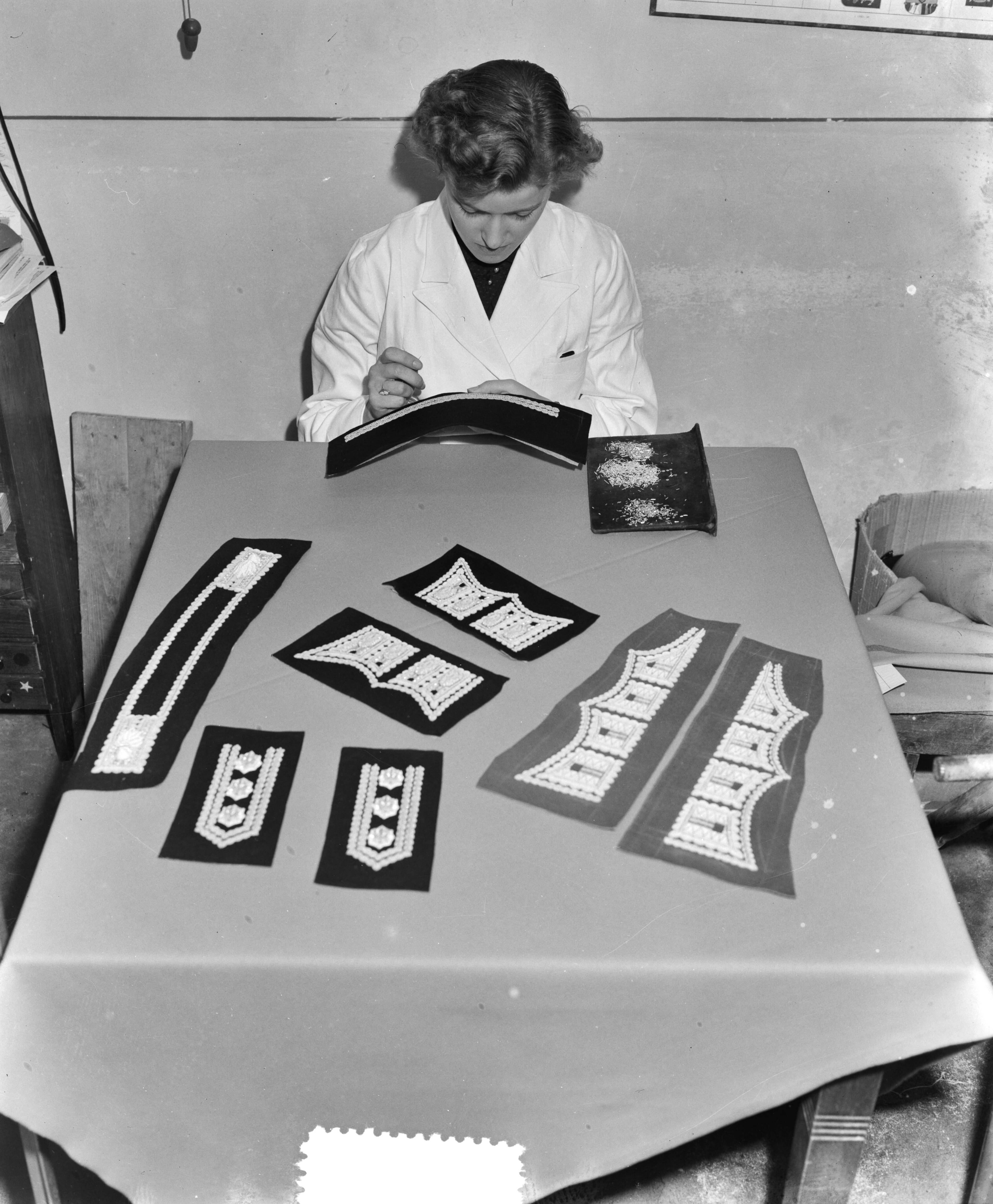 Fotocollectie Anefo — Bredase meisjes werken in Breda aan Engelse koningskleding. Het vervaardigen van borduursels voor de manchetsluitstukken voor de Welsh Guards — Foto: Duinen, G.W. van / Anefo. Licentie: Set B: Rechtenvrij / Publiek Domein. Bron: Nationaal Archief. http://hdl.handle.net/10648/a9054ed2-d0b4-102d-bcf8-003048976d84