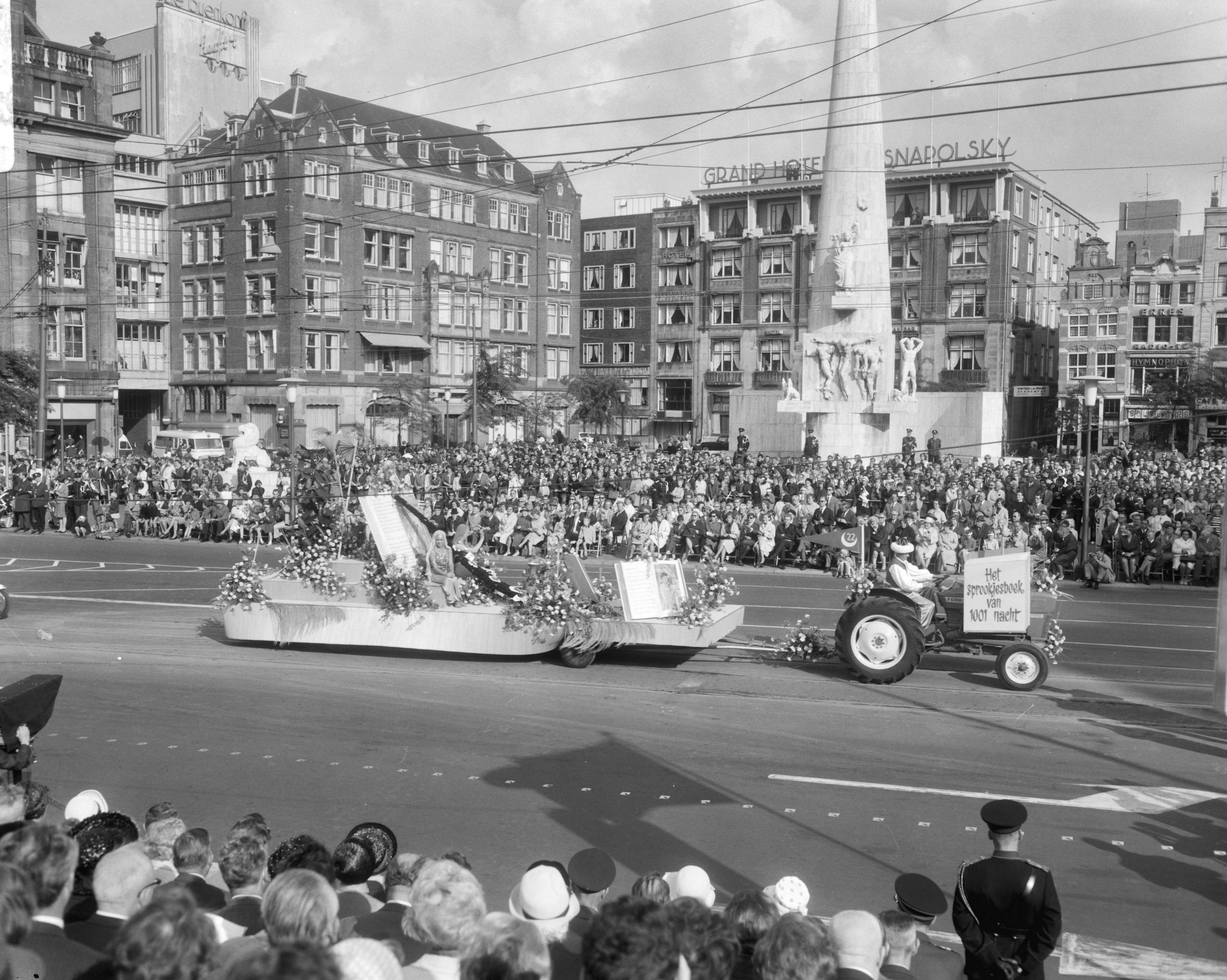 Bloemencorso van Aalsmeer te Amsterdam — Een praalwagen bij de Dam te Amsterdam met op de achtergrond het Nationaal Monument — Foto: Bilsen, Joop van / Anefo. Licentie: Set B: Rechtenvrij / Publiek Domein. Bron: Nationaal Archief. http://hdl.handle.net/10648/aafaf052-d0b4-102d-bcf8-003048976d84