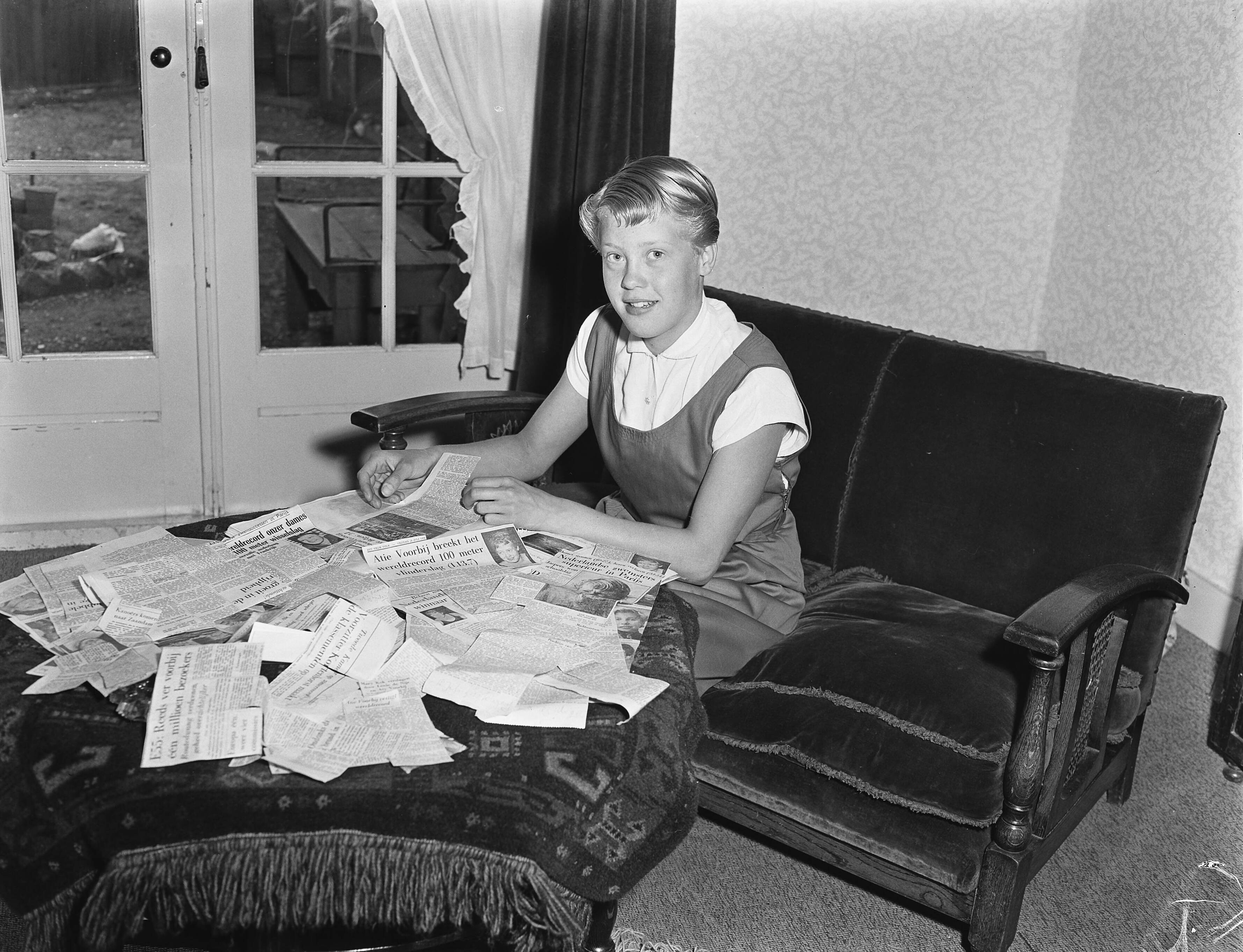Reportage Atie Voorbij (zwemkampioene) — Atie Voorbij (14-jarige zwemkampioene). Atie met op tafel een grote hoeveelheid krantenknipsels met berichten over haar prestaties — Foto: Pot, Harry / Anefo. Licentie: Set B: Rechtenvrij / Publiek Domein. Bron: Nationaal Archief. http://hdl.handle.net/10648/a938922e-d0b4-102d-bcf8-003048976d84