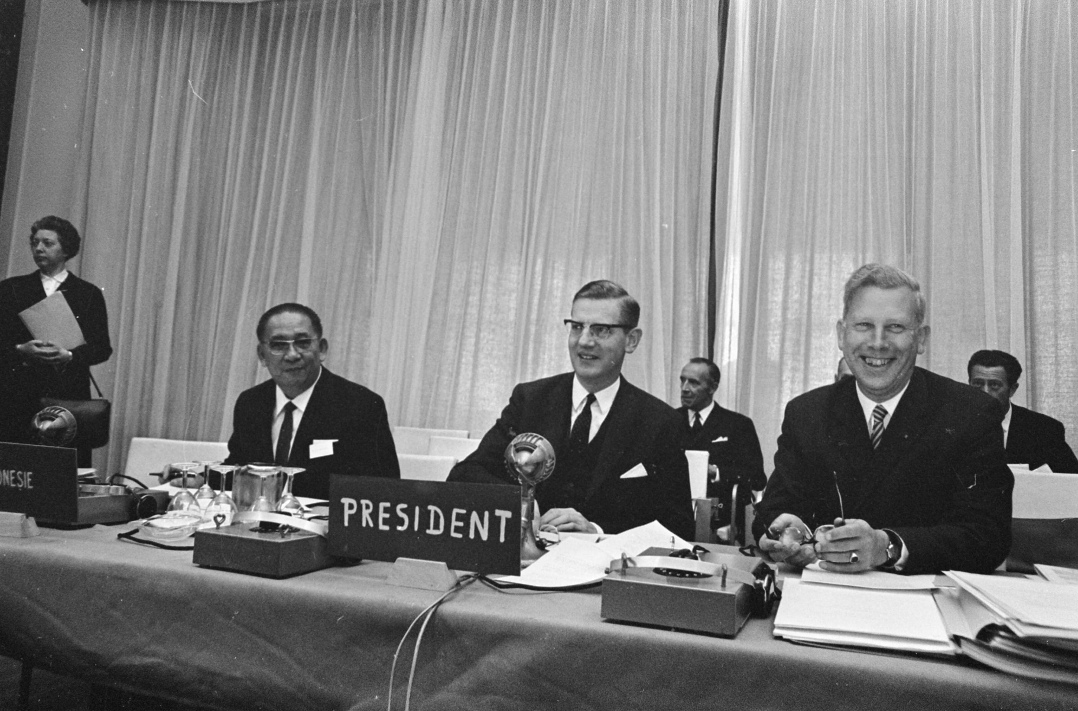 Conferentie van de Intergouvernementele Groep te Scheveningen — Voorzitter minister (zonder portefeuille) Berend-Jan Udink, links naast hem mr. H. A. Pandelaki , rechts dhr. J. Everts — Foto: Fotograaf Onbekend / Anefo. Licentie: Set B: Rechtenvrij / Publiek Domein. Bron: Nationaal Archief. http://hdl.handle.net/10648/ab1c972a-d0b4-102d-bcf8-003048976d84