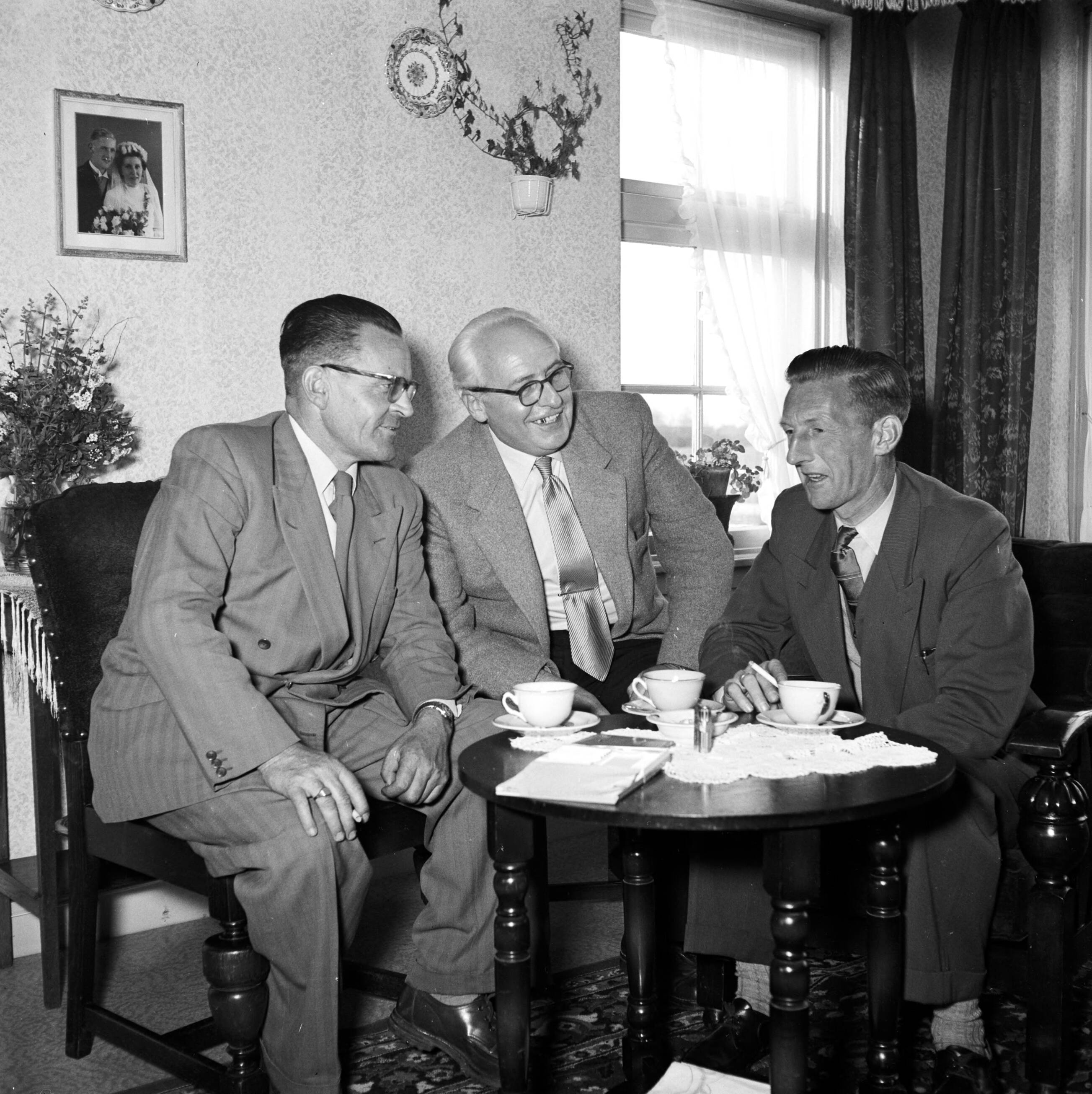 Fotocollectie Van de Poll — Gerard de Jong in gesprek met Ynse Postma en de fotograaf Willem van de Poll. Aan de wand een trouwfoto van het echtpaar De Jong — Foto: Poll, Willem van de. Licentie: Set B: Rechtenvrij / Publiek Domein. Bron: Nationaal Archief. http://hdl.handle.net/10648/aecce96a-d0b4-102d-bcf8-003048976d84