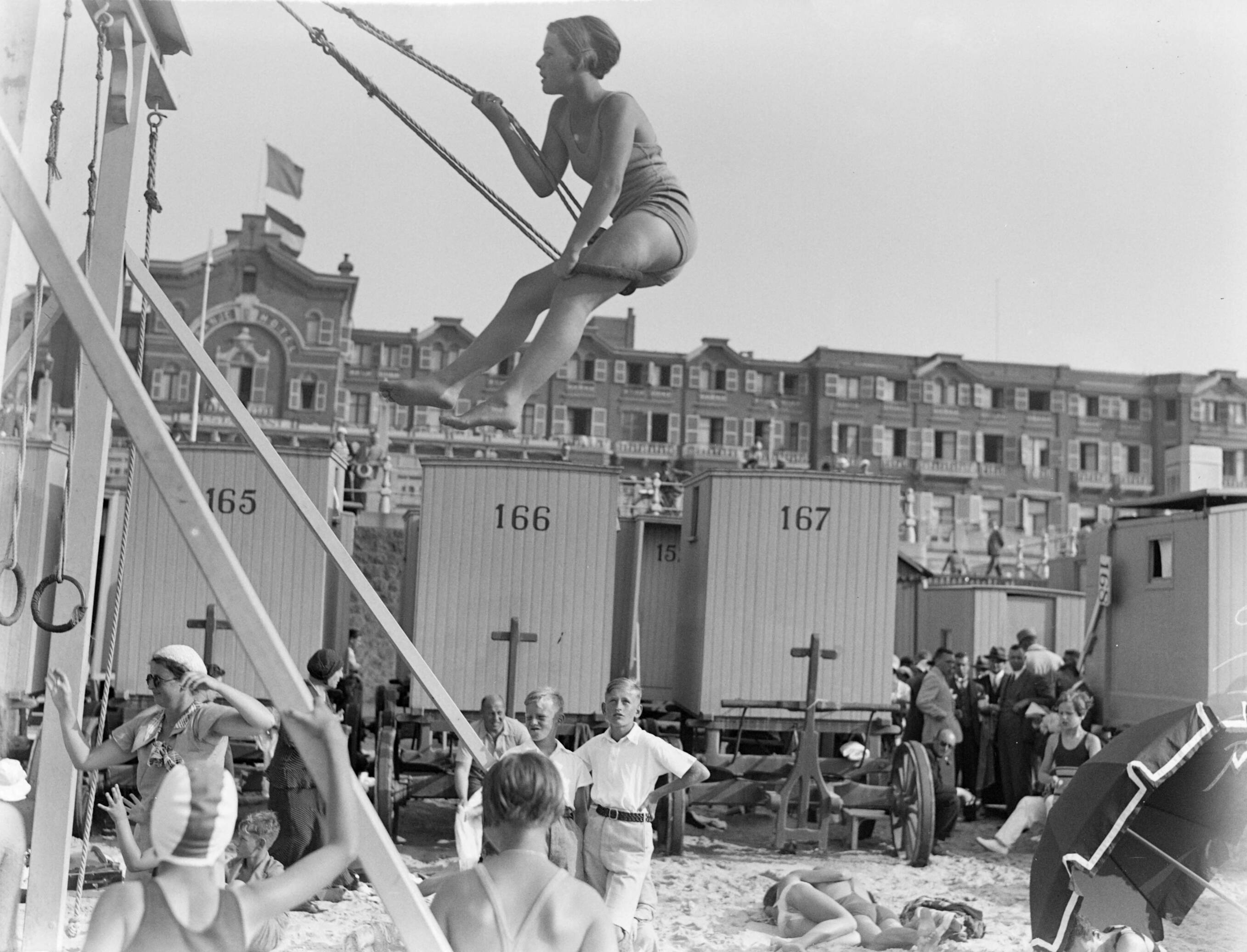 Scheveningen. — Schommelen op het strand in Scheveningen voor het Palace Hotel. Op de achtergrond badkoetsen. — Foto: Poll, Willem van de. Licentie: Set B: Rechtenvrij / Publiek Domein. Bron: Nationaal Archief. http://hdl.handle.net/10648/ae9ac57a-d0b4-102d-bcf8-003048976d84