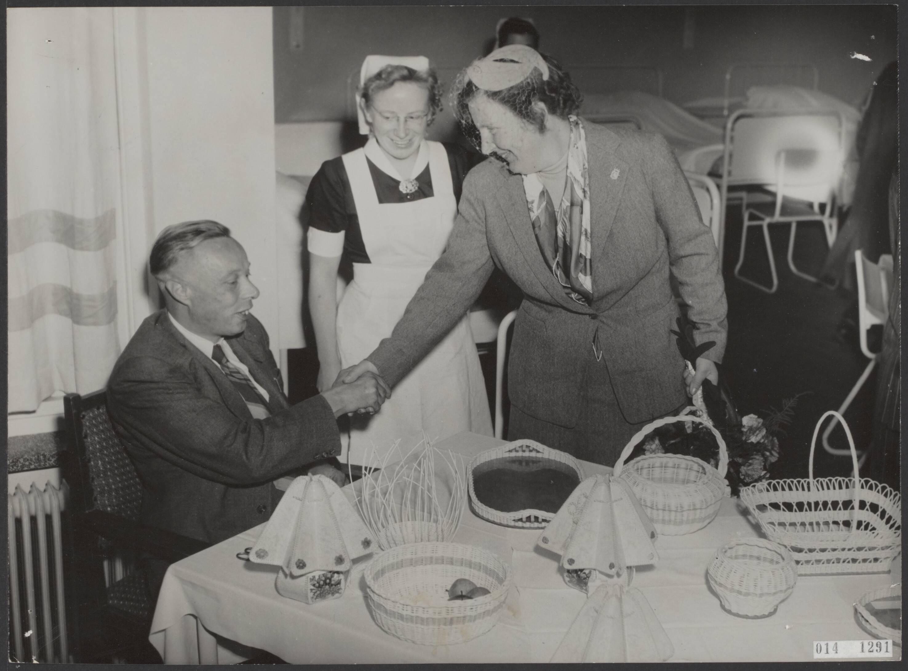 Fotocollectie Elsevier Binnenland — Opening van het verpleeghuis "Der Boede"te Koudekerke op Walcheren door koningin Juliana. In het rusthuis werd aan de koningin door een der patiënten, de heer W. Lente, gevlochten pitrietwerk voor de prinsesjes aangeboden — Foto: Fotograaf Onbekend / Anefo. Licentie: Set B: Rechtenvrij / Publiek Domein. Bron: Nationaal Archief. http://hdl.handle.net/10648/adb353e8-d0b4-102d-bcf8-003048976d84