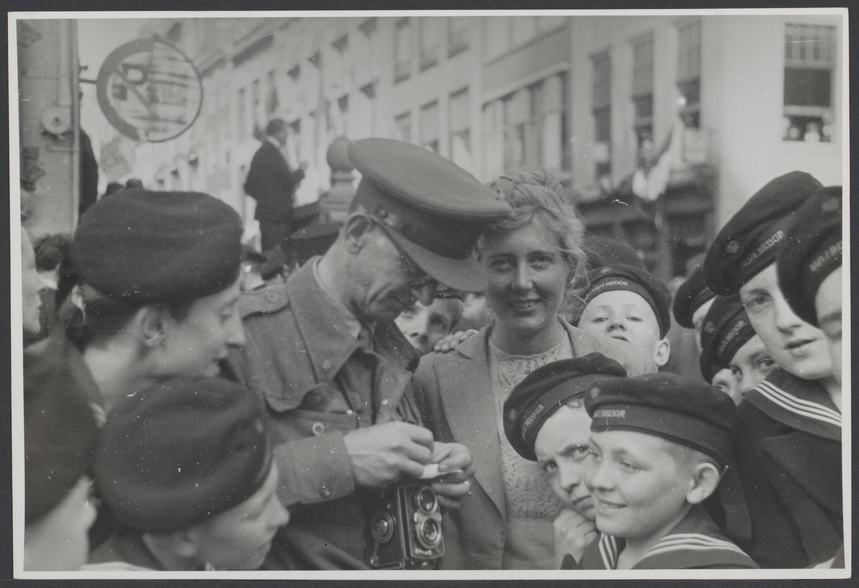 Bevrijding 's Gravenhage (Den Haag) — Canadese militair (fotocamera op de buik) rolt een shaggie te midden van uitgelaten bevolking, tijdens de intocht van de Canadezen bij de bevrijding van Den Haag — Foto: Wal, J.Th. A. van der / Spaarnestad. Licentie: Set B: Rechtenvrij / Publiek Domein. Bron: Nationaal Archief. http://hdl.handle.net/10648/6902dd8f-fc07-9b0d-e0d4-55df1a9a3e8e
