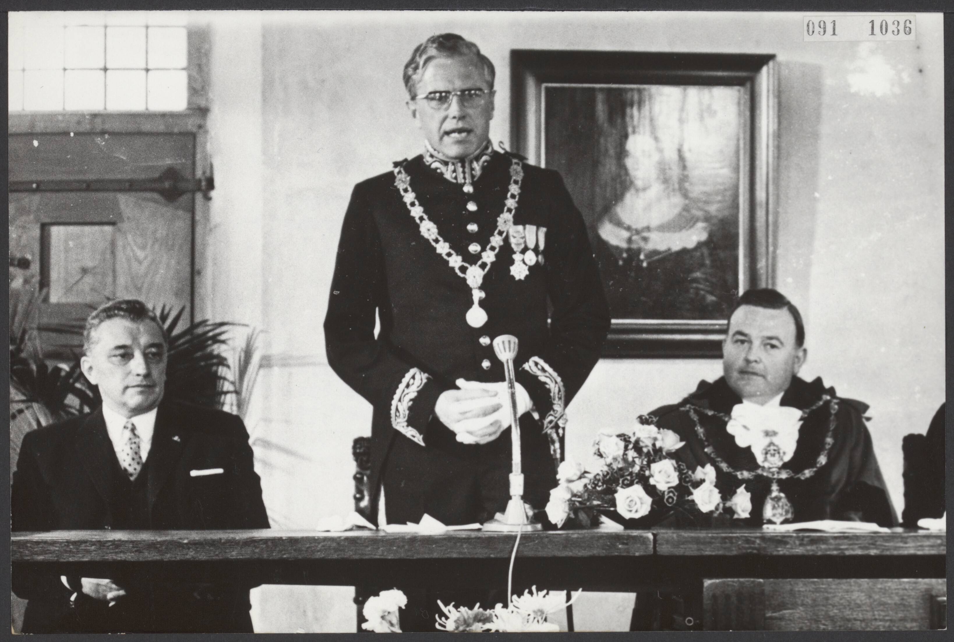 Fotocollectie Elsevier Binnenland — In de burgerzaal in het stadhuis van Middelburg is een herdenkingsbijeenkomst t.g.v. het 750-jarig bestaan gehouden. Burgemeester mr. J. Drijber tijdens zijn openingswoord. Naast hem rechts de Commissaris der Koningin In de provincie Zeeland mr. J. van Aartsen en geheel rechts de burgemeester van de Engelse plaats Folkstone, waarmee Middelburg sinds 1951 een stedenband heeft. De gouden keten om de hals van de Engelse burgemeester is van puur goud en heeft een waarde van 60.000 gulden — Foto: Nijs, Jac. de / Anefo. Licentie: Set B: Rechtenvrij / Publiek Domein. Bron: Nationaal Archief. http://hdl.handle.net/10648/ae21c120-d0b4-102d-bcf8-003048976d84