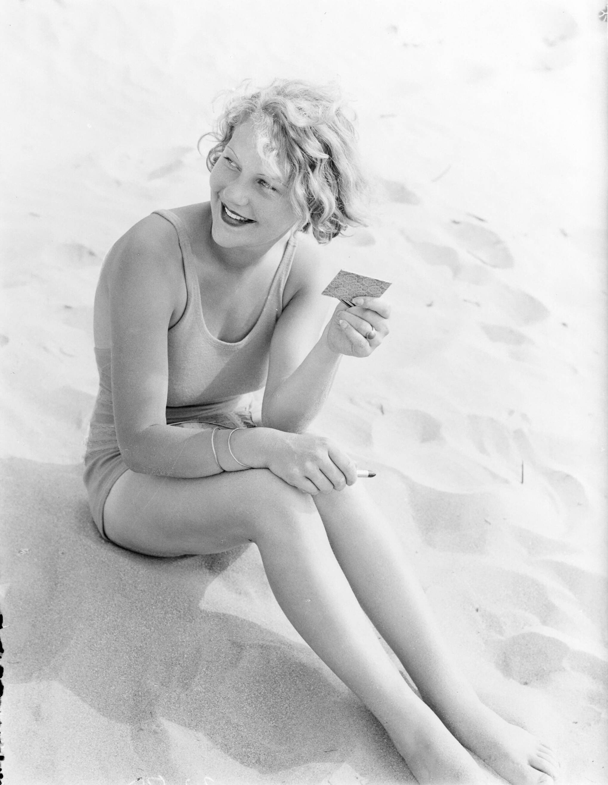 Reportage fotomodel — Model Eva Waldschmidt zit in het zand met spiegeltje en lippenstift — Foto: Poll, Willem van de. Licentie: Set B: Rechtenvrij / Publiek Domein. Bron: Nationaal Archief. http://hdl.handle.net/10648/aea7fa1a-d0b4-102d-bcf8-003048976d84