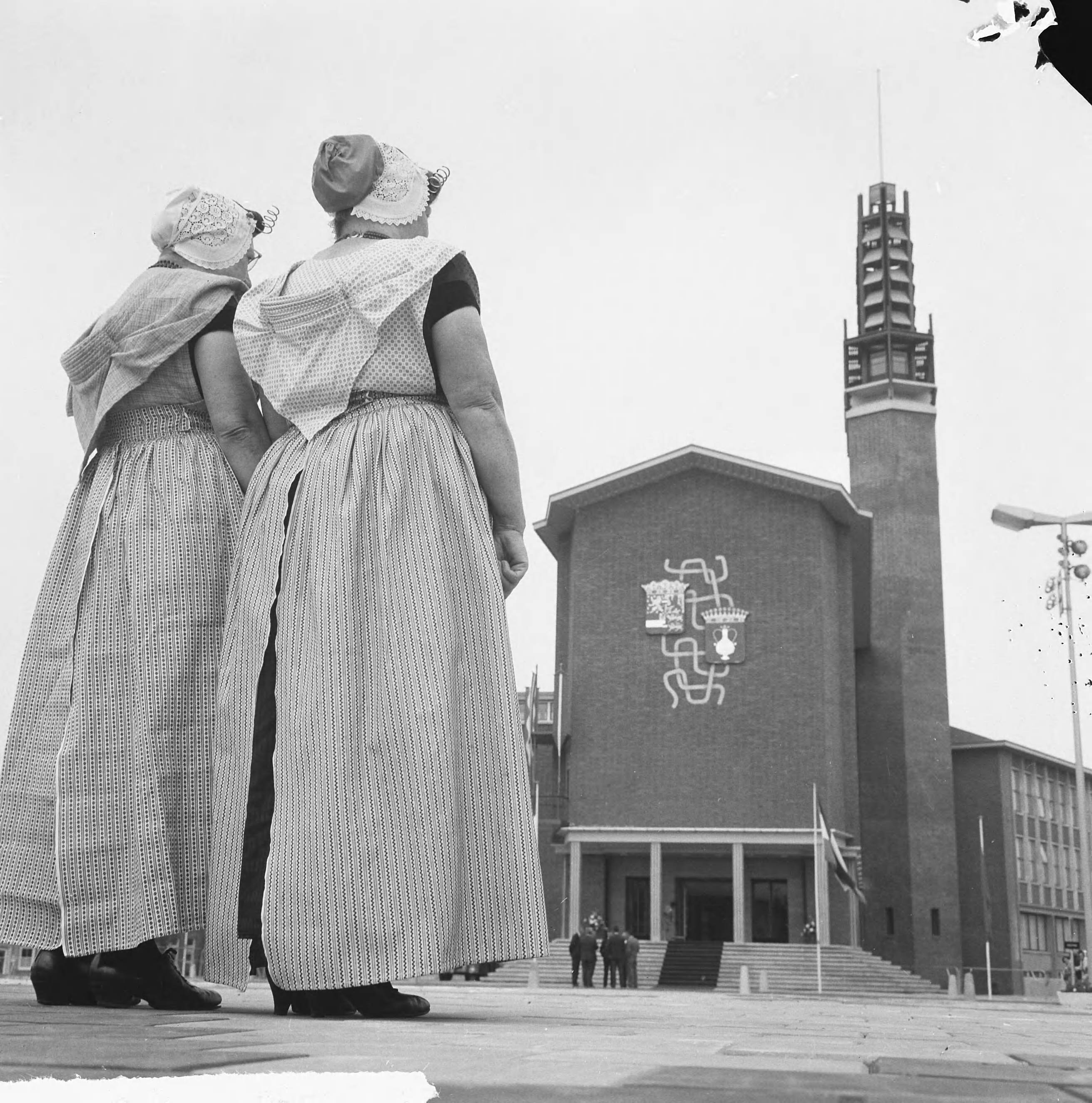Koningin Juliana opent het nieuwe stadhuis te Vlissingen — Twee vrouwen in Klederdracht staan voor het nieuwe stadhuis — Foto: Nijs, Jac. de / Anefo. Licentie: Set B: Rechtenvrij / Publiek Domein. Bron: Nationaal Archief. http://hdl.handle.net/10648/aaa9a1fc-d0b4-102d-bcf8-003048976d84