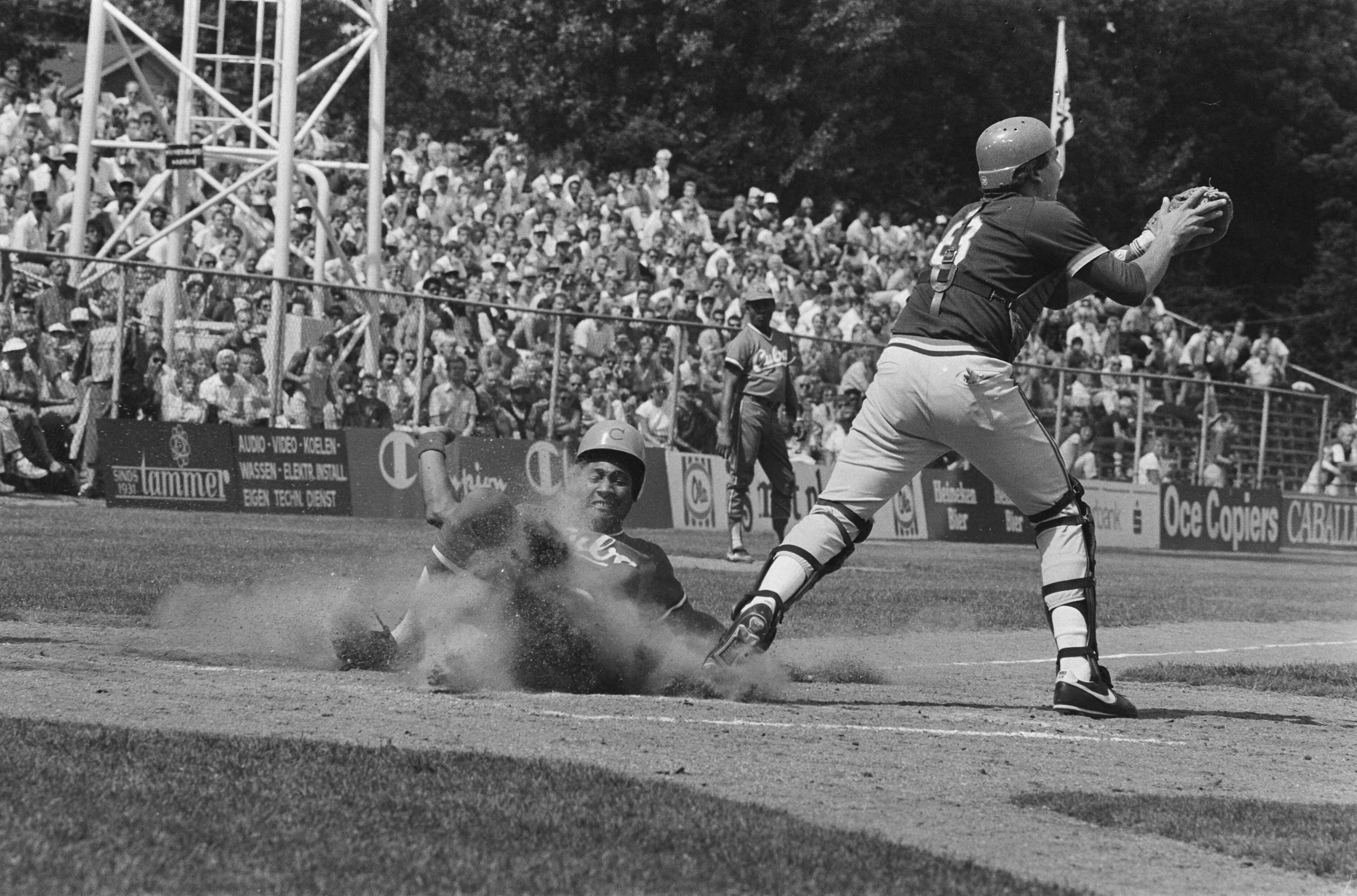 Fotocollectie Anefo — Wereldkampioenschappen honkbal in Haarlem tussen Cuba en Puerto Rico ; Lourdes Gurriel scoort voor Cuba zesde punt, rechts catcher Jose Lorenzana van Porto Rico — Foto: Bogaerts, Rob / Anefo. Licentie: Set B: Rechtenvrij / Publiek Domein. Bron: Nationaal Archief. http://hdl.handle.net/10648/ad558c9a-d0b4-102d-bcf8-003048976d84